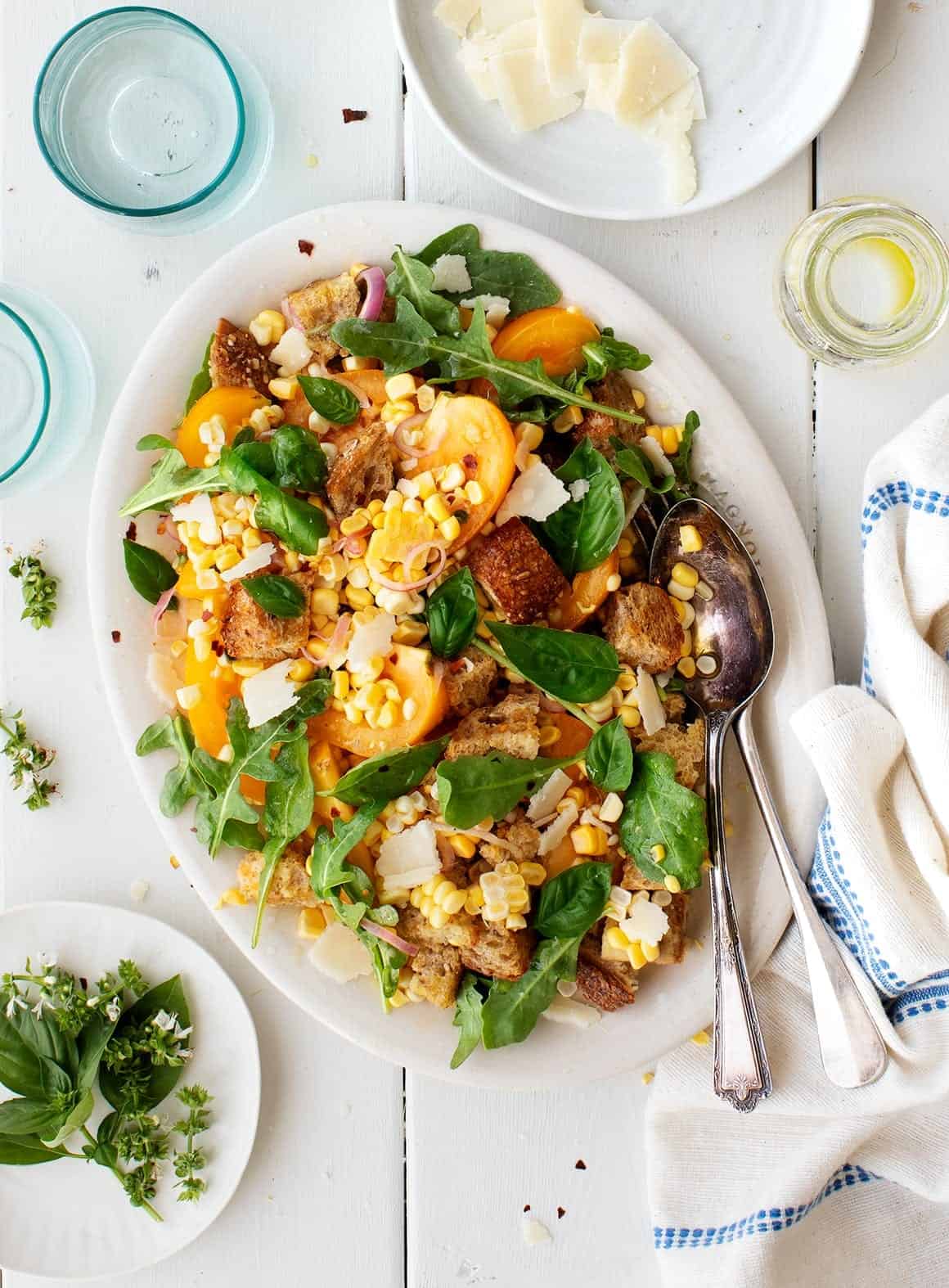 Sweet Corn & Arugula Panzanella on a platter with utensils