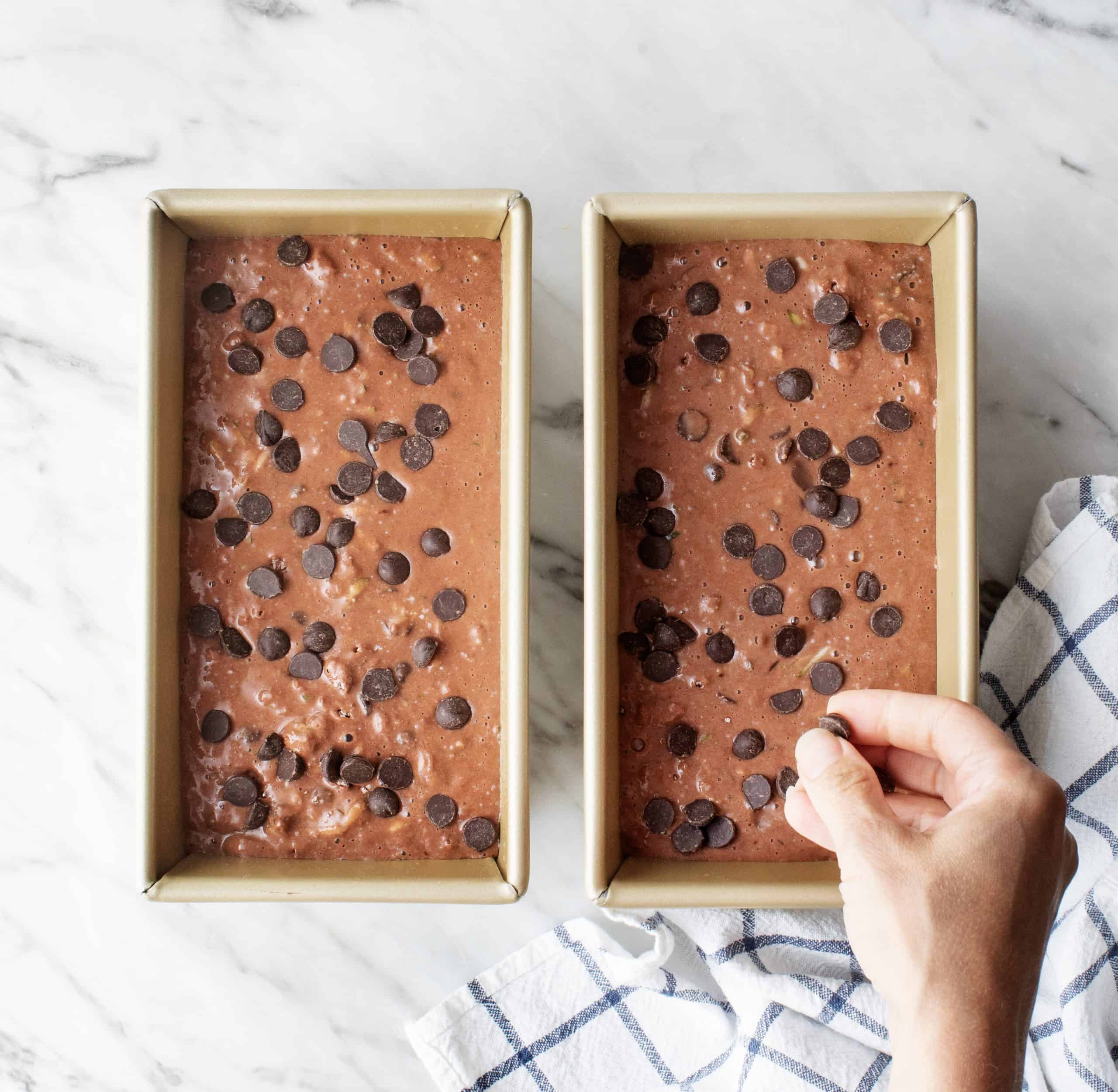 Hand sprinkling chocolate chips over chocolate zucchini bread batter in loaf pans