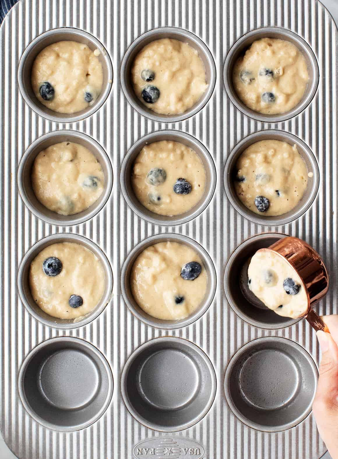 Hand using measuring cup to scoop batter into muffin tins