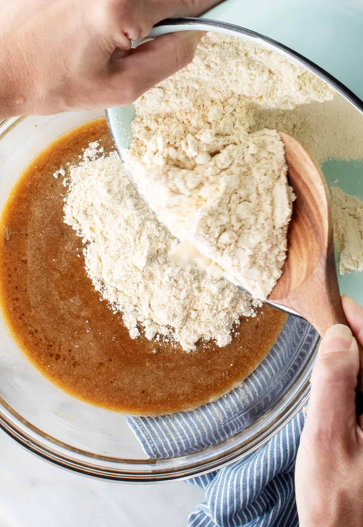Hands pouring bowl of dry ingredients into bowl of wet ingredients