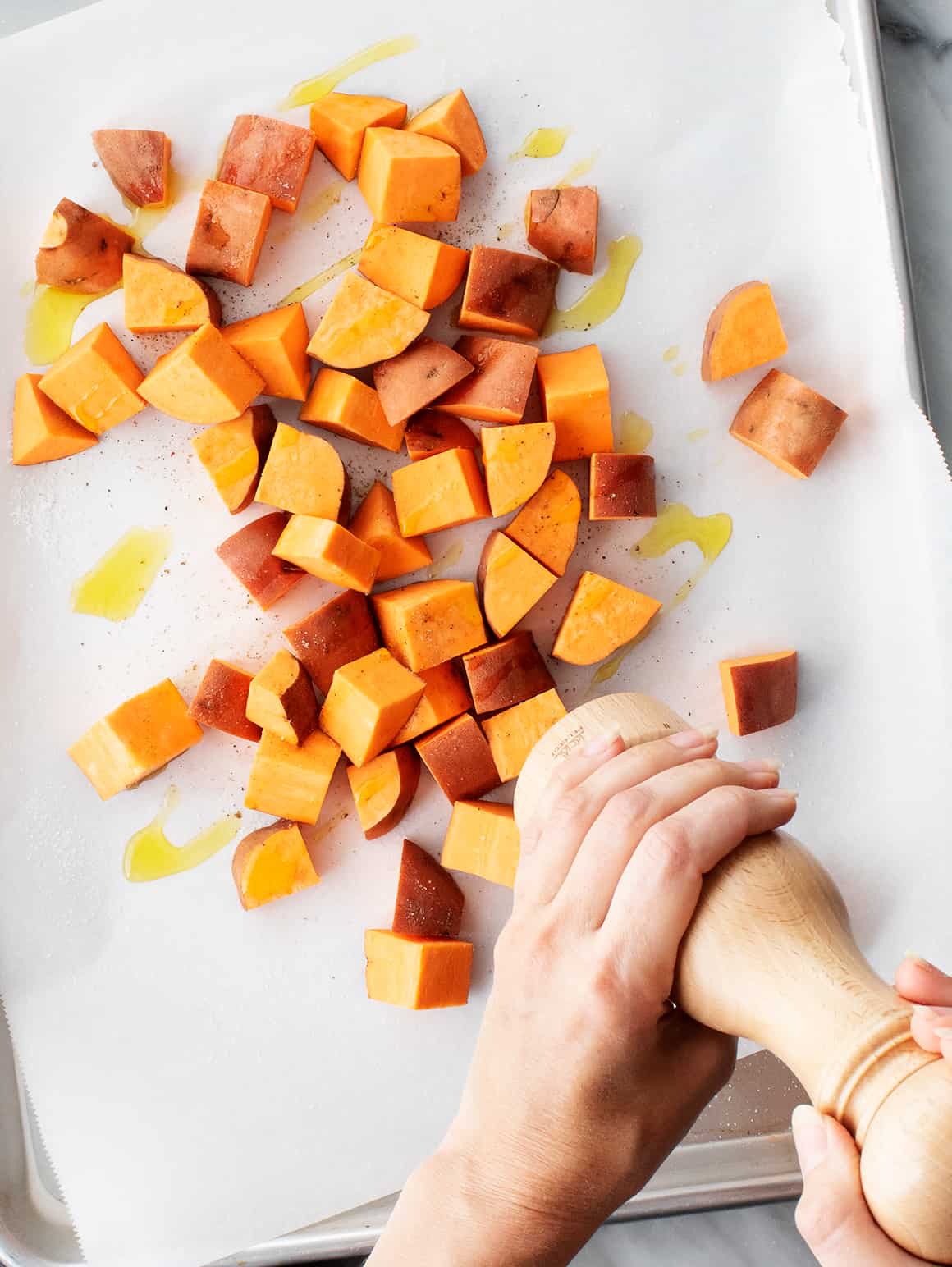 Hands seasoning sweet potato cubes with black pepper