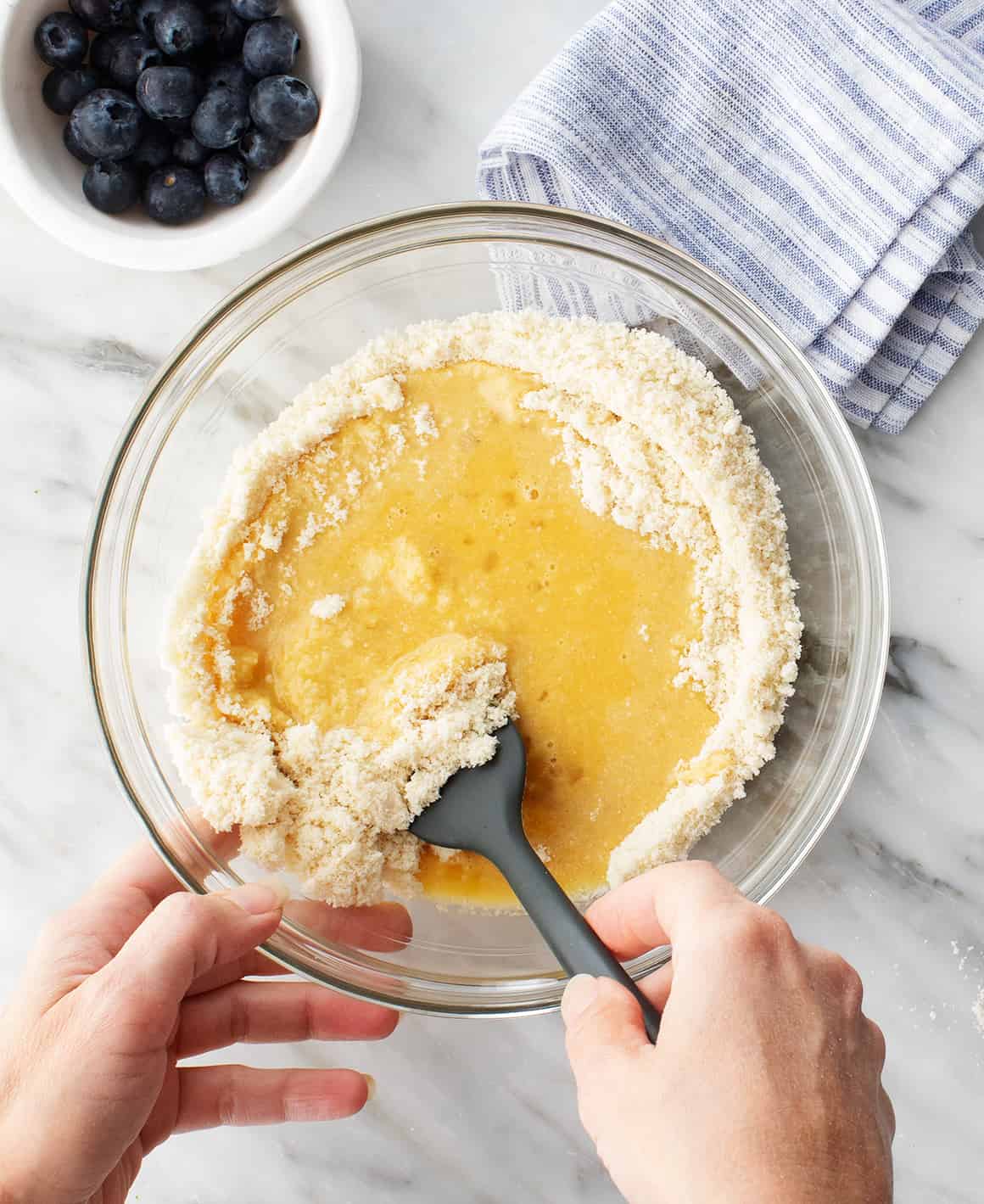 Hand mixing wet and dry ingredients in a mixing bowl with spatula