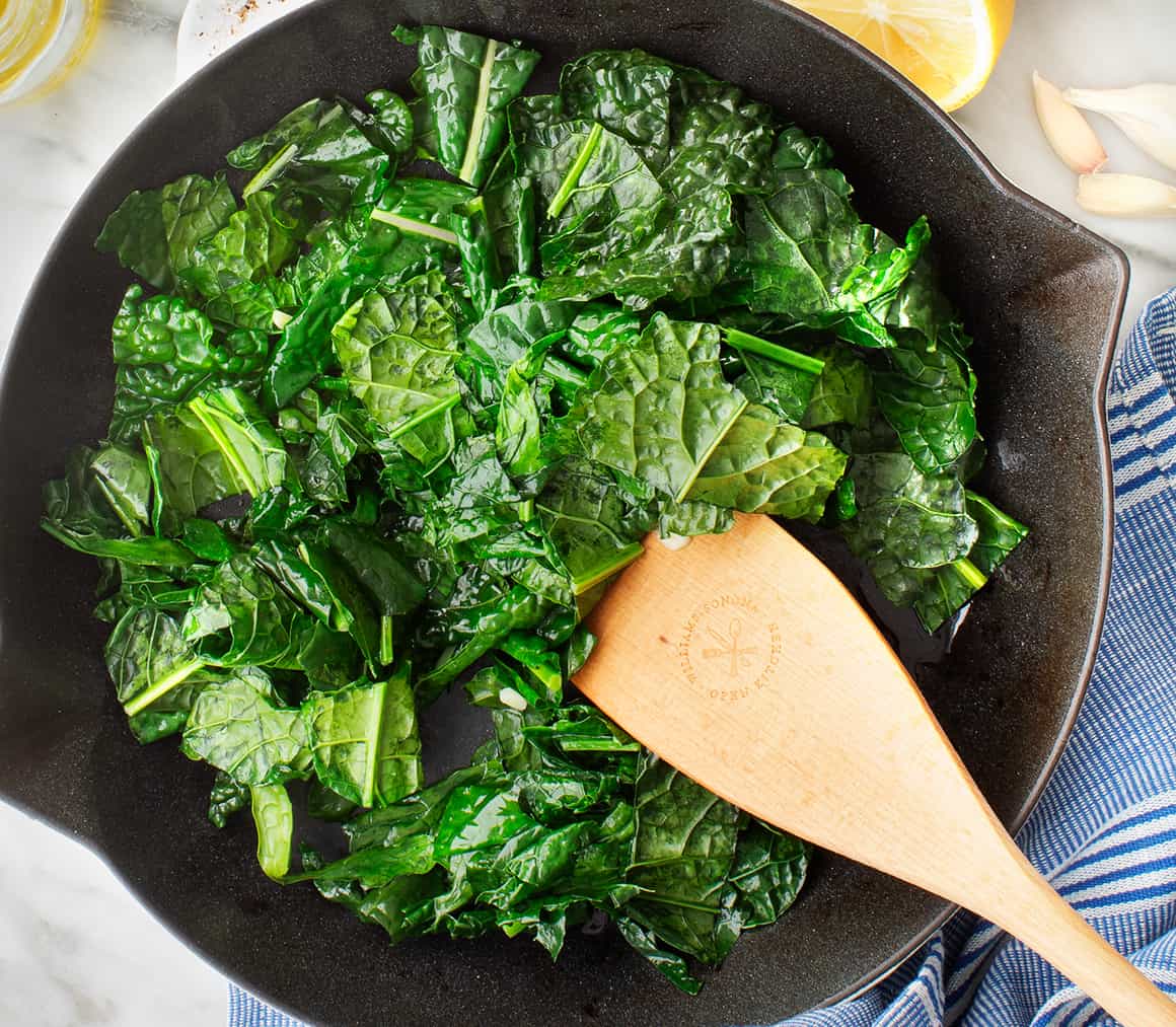 Sauteed kale in a skillet with wooden spatula