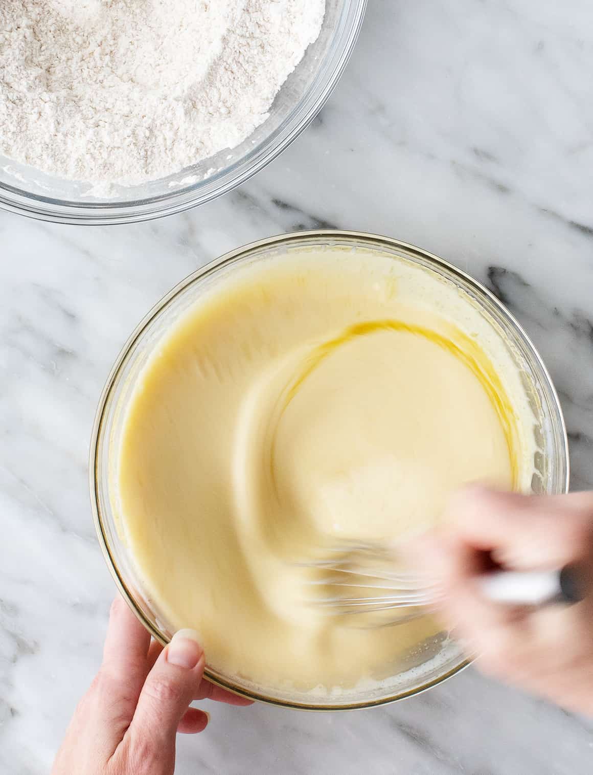Hands whisking wet ingredients in a mixing bowl
