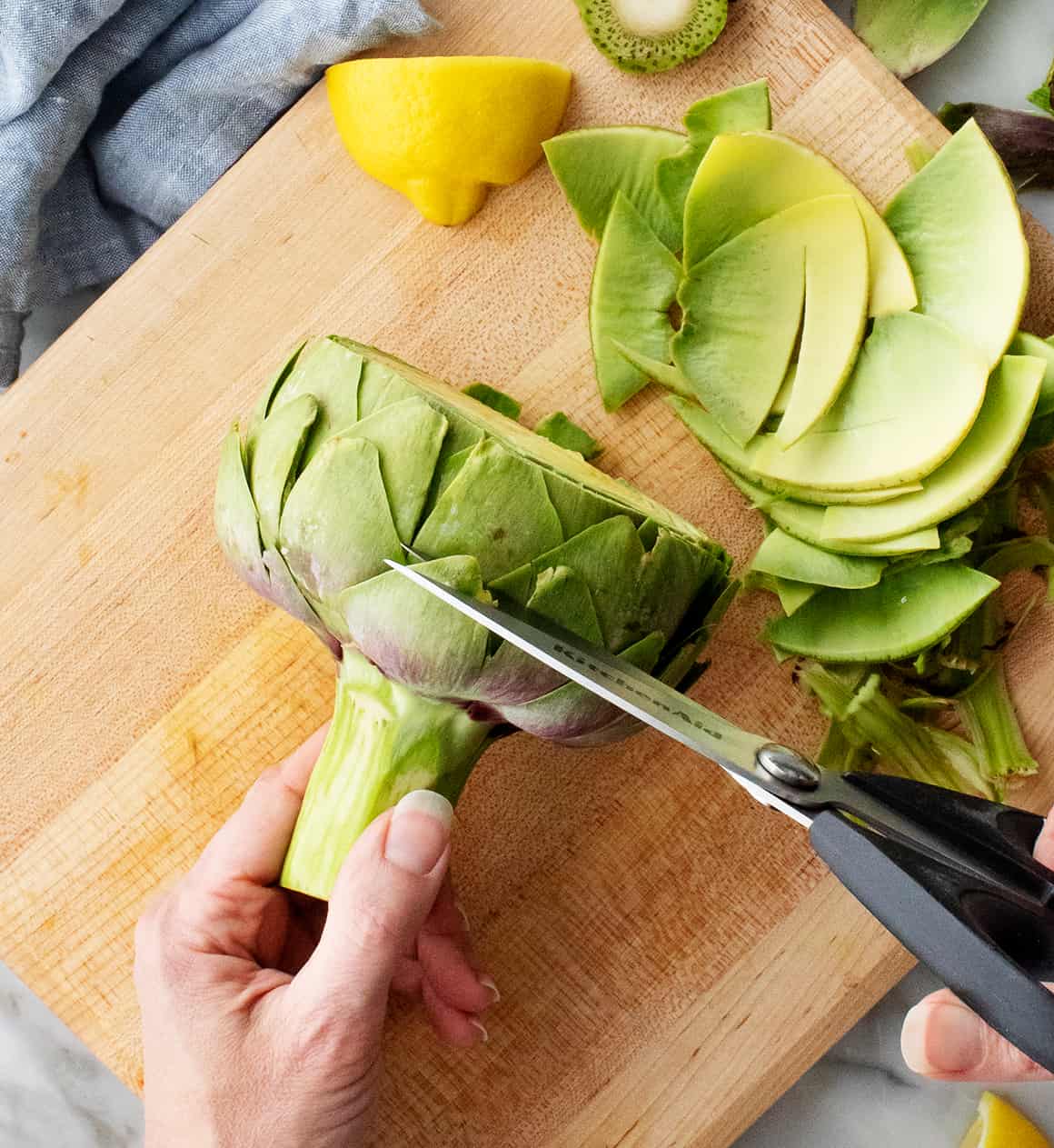 Hands trimming thorny artichoke petals with kitchen shears