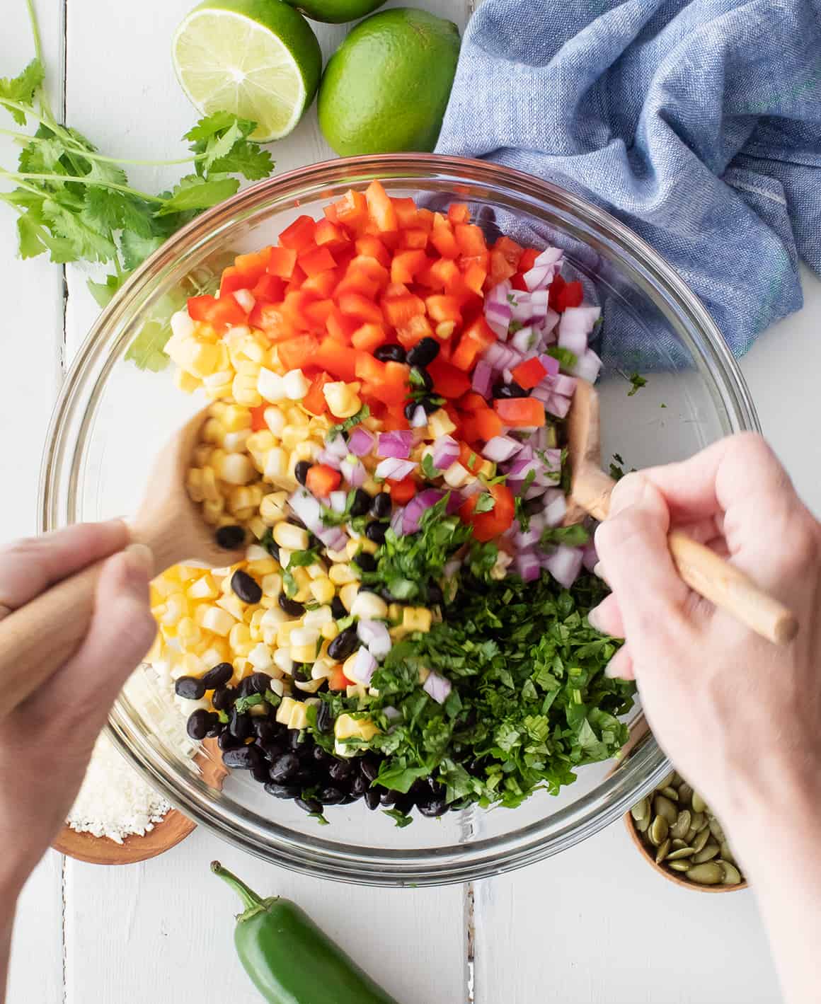 Hands tossing salad in bowl with wooden spoons