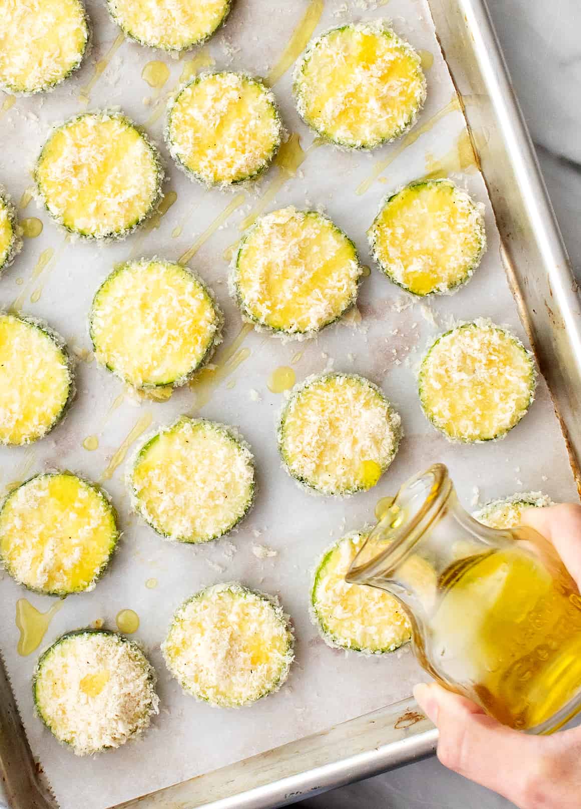 Hand drizzling tray of air fryer zucchini chips with olive oil