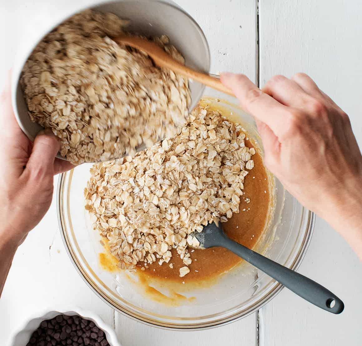 Pouring oats into peanut butter mixture in a mixing bowl