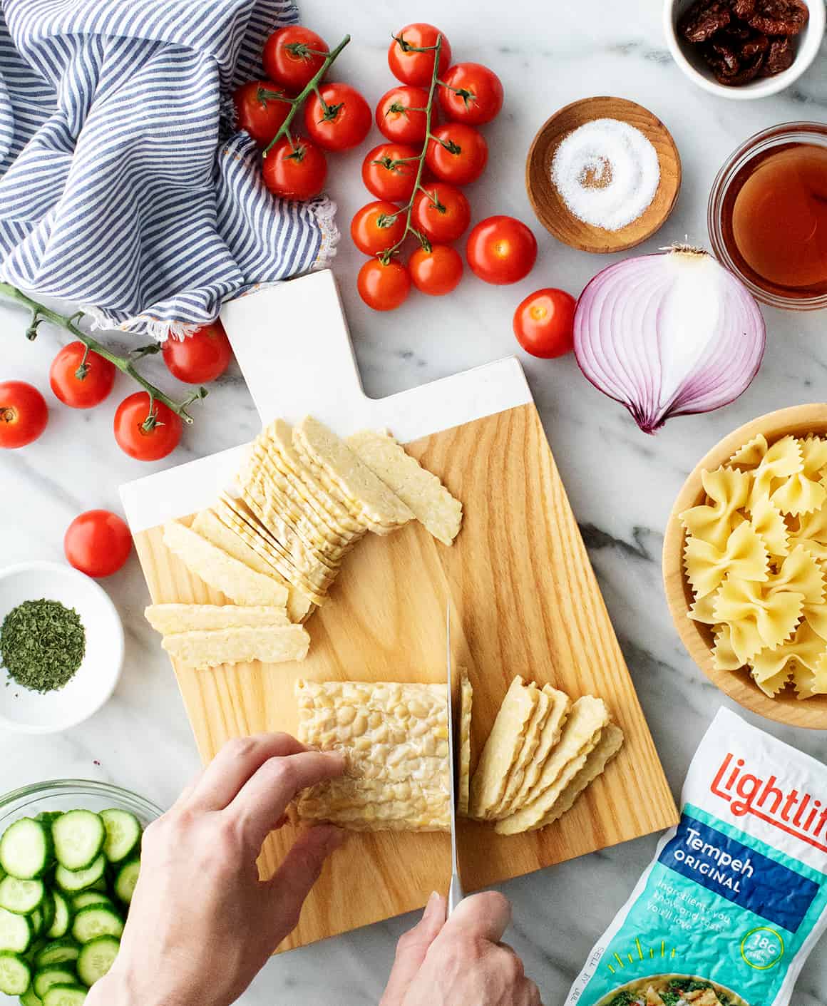Hand slicing tempeh on cutting board with knife