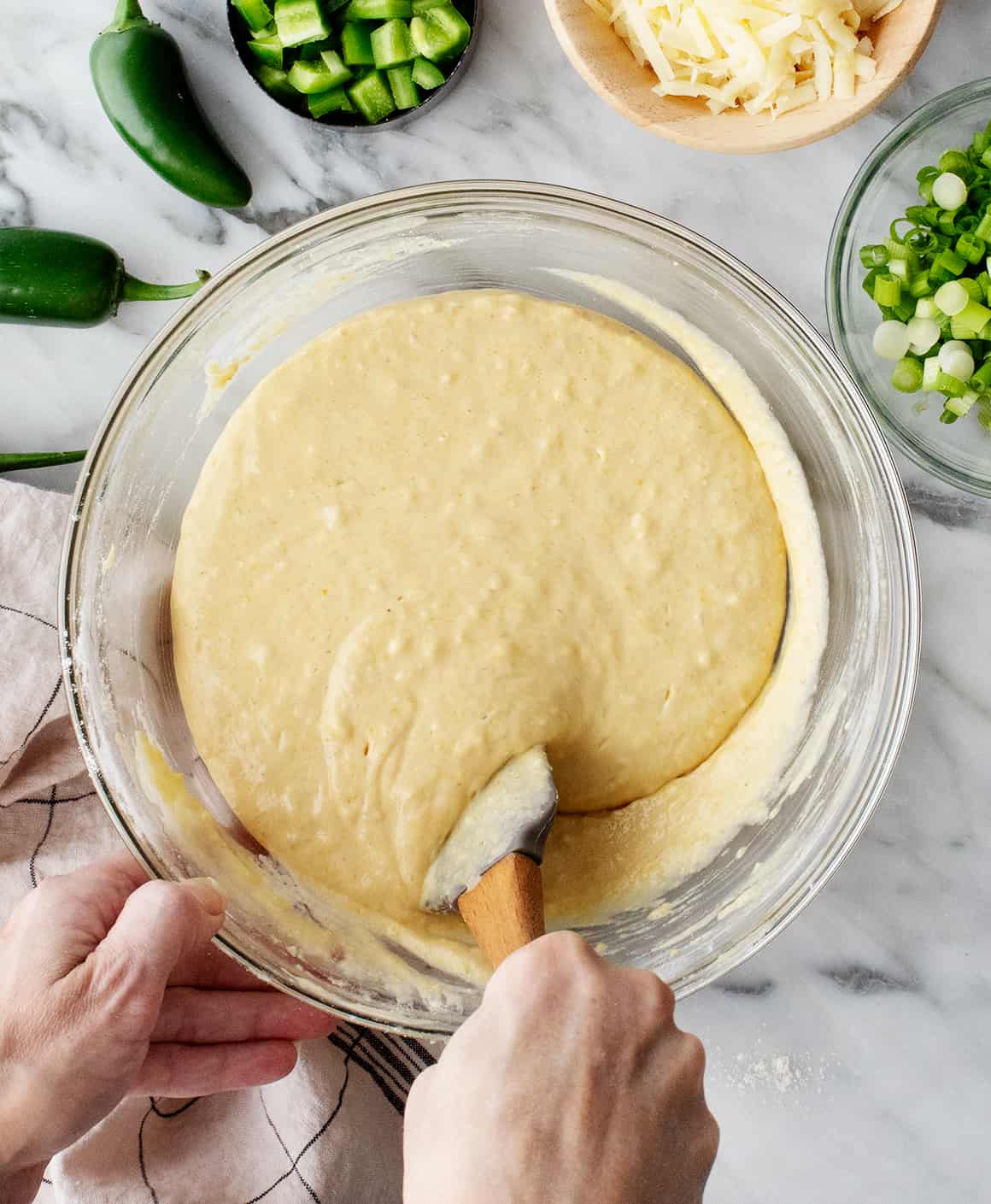 Hand folding cornbread batter in large bowl with rubber spatula