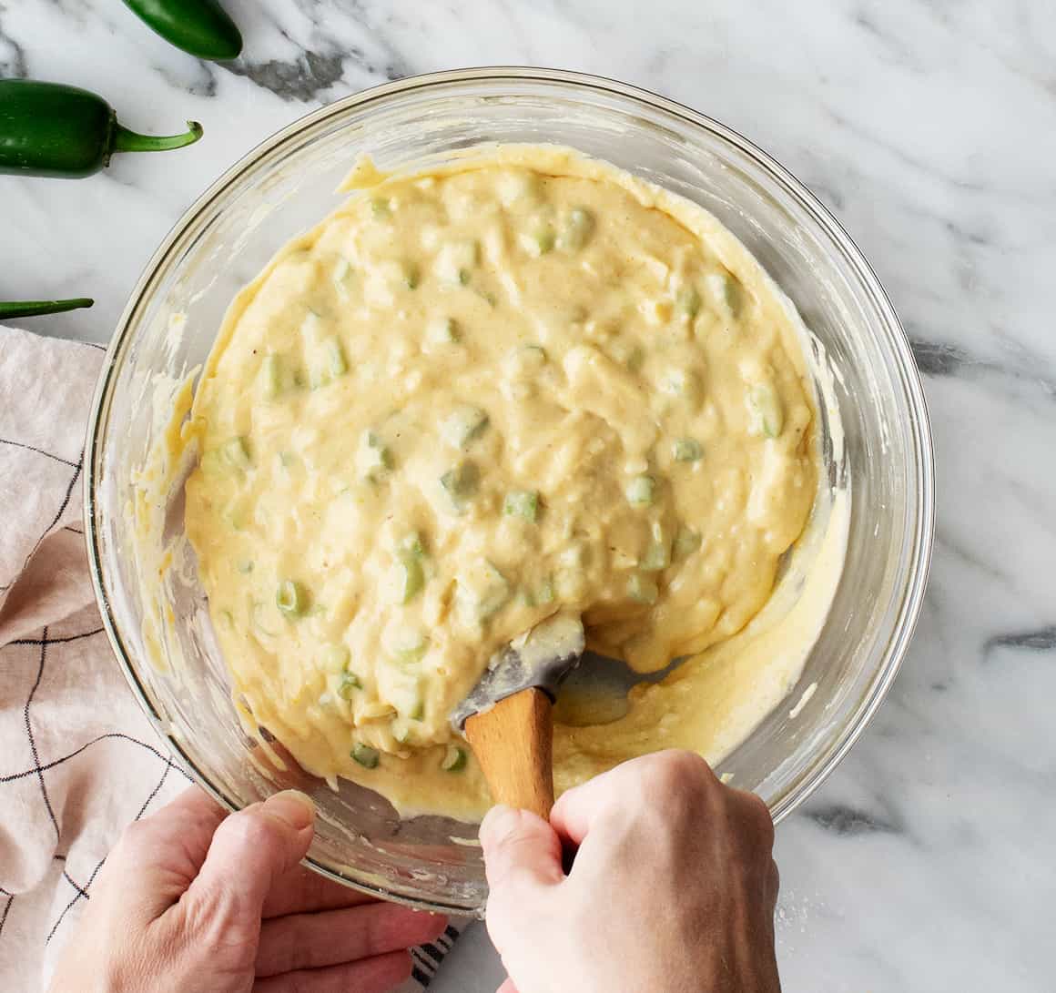 Hand mixing bowl of jalapeno cornbread batter with rubber spatula