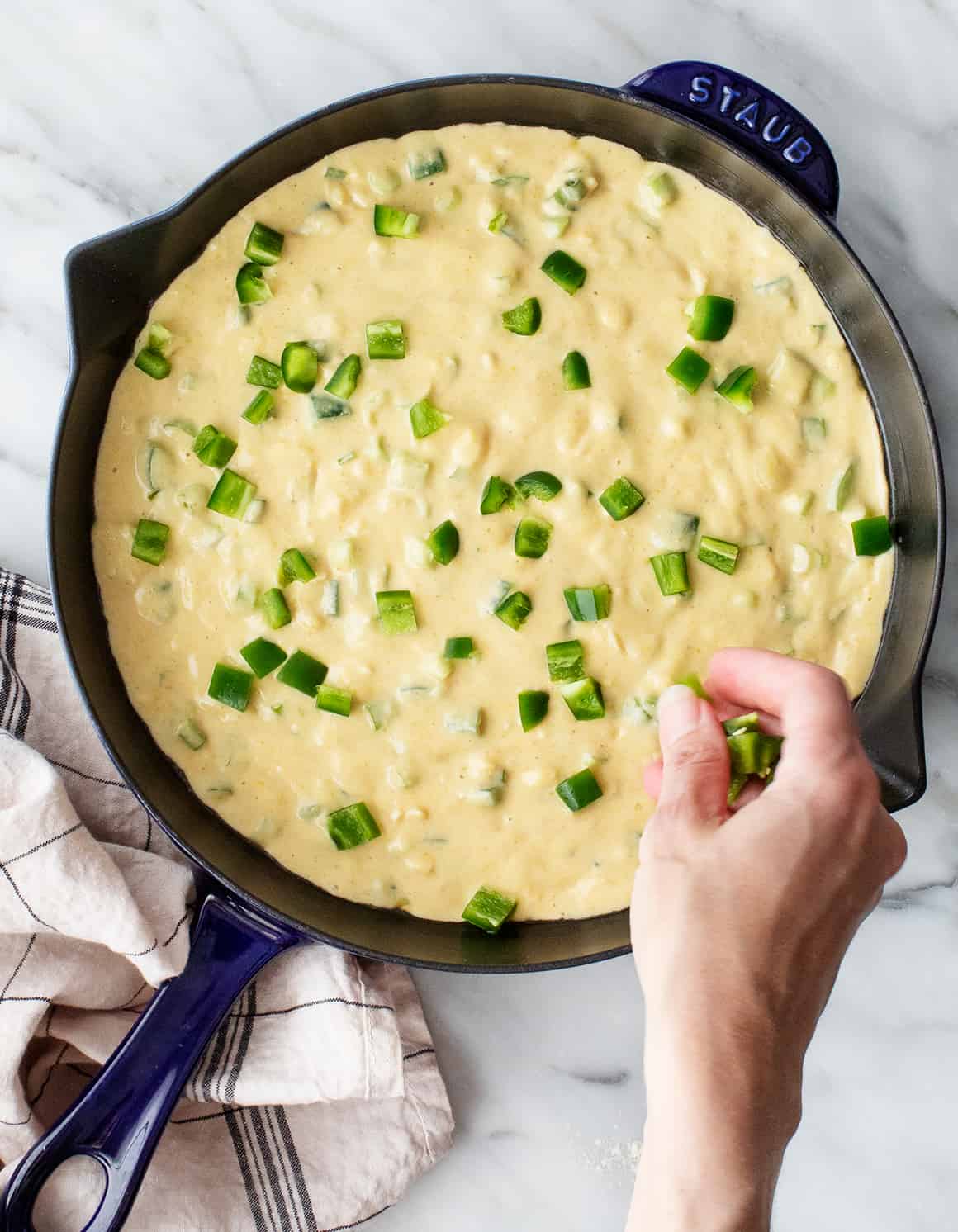 Sprinkling diced jalapenos over cornbread batter in skillet