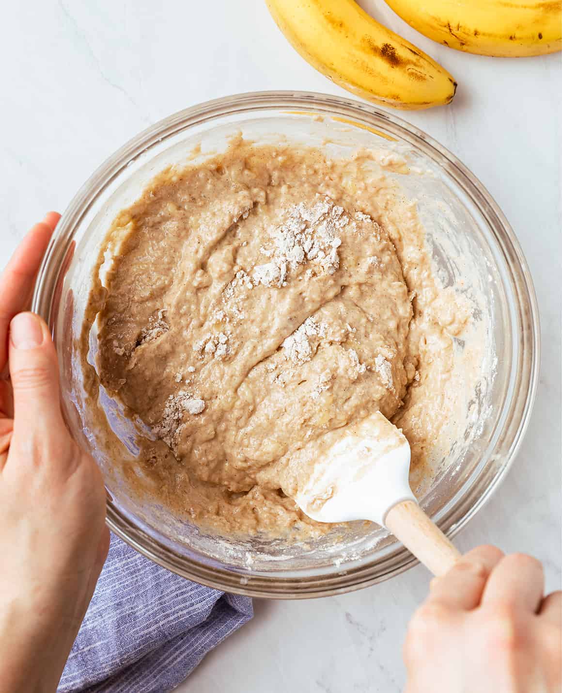 Hands using spatula to mix pancake batter in a large bowl