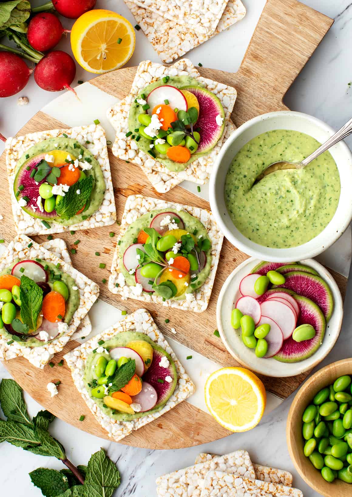 Platter of rice crisps with herbed white bean spread, radishes, carrots, feta, and microgreens