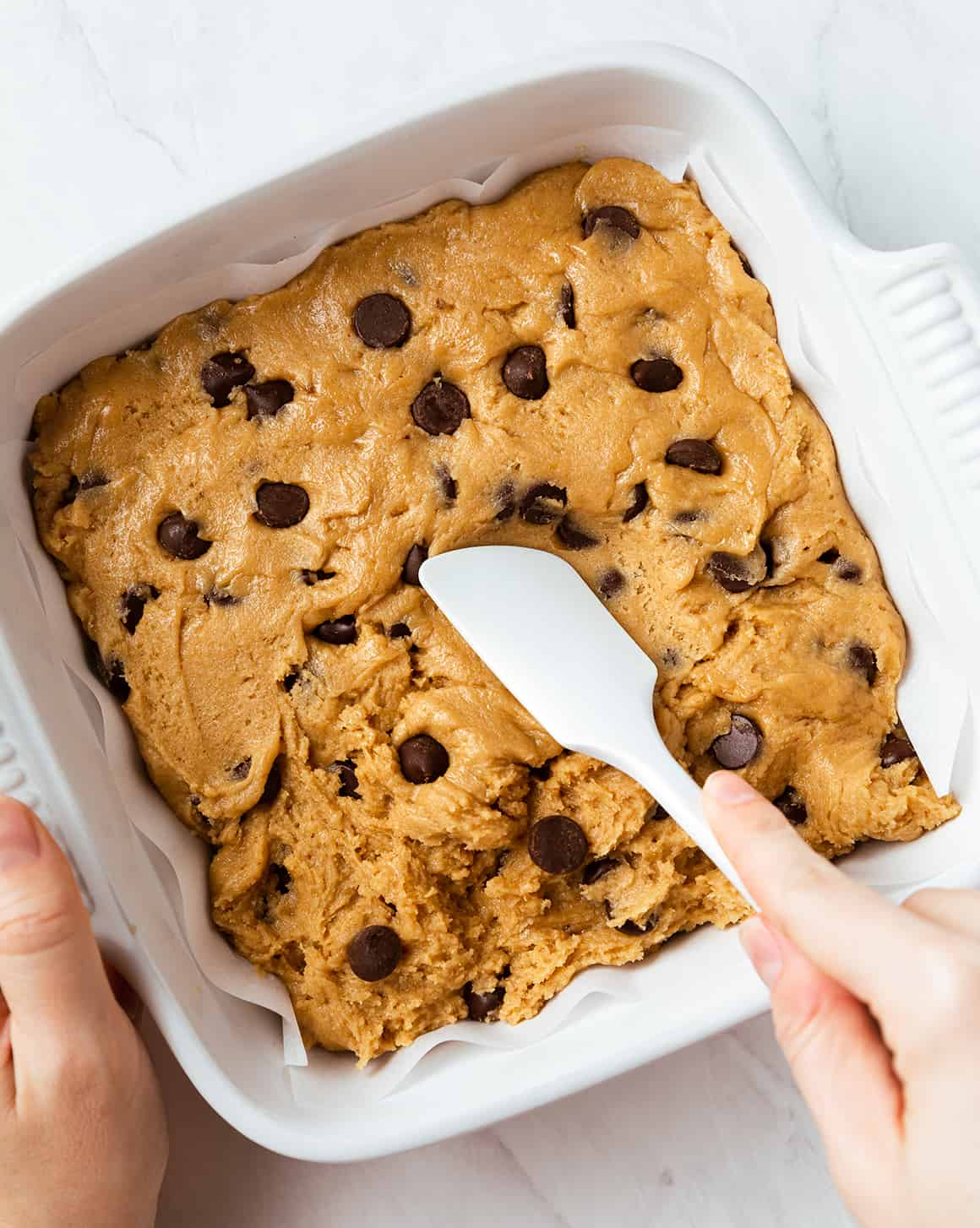 Hand using spatula to press cookie dough into baking dish