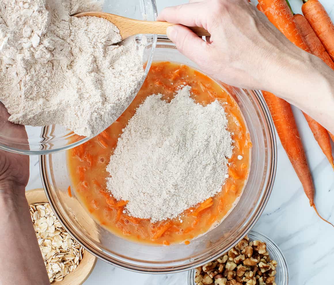 Hands using spatula to add dry ingredients to bowl of wet ingredients