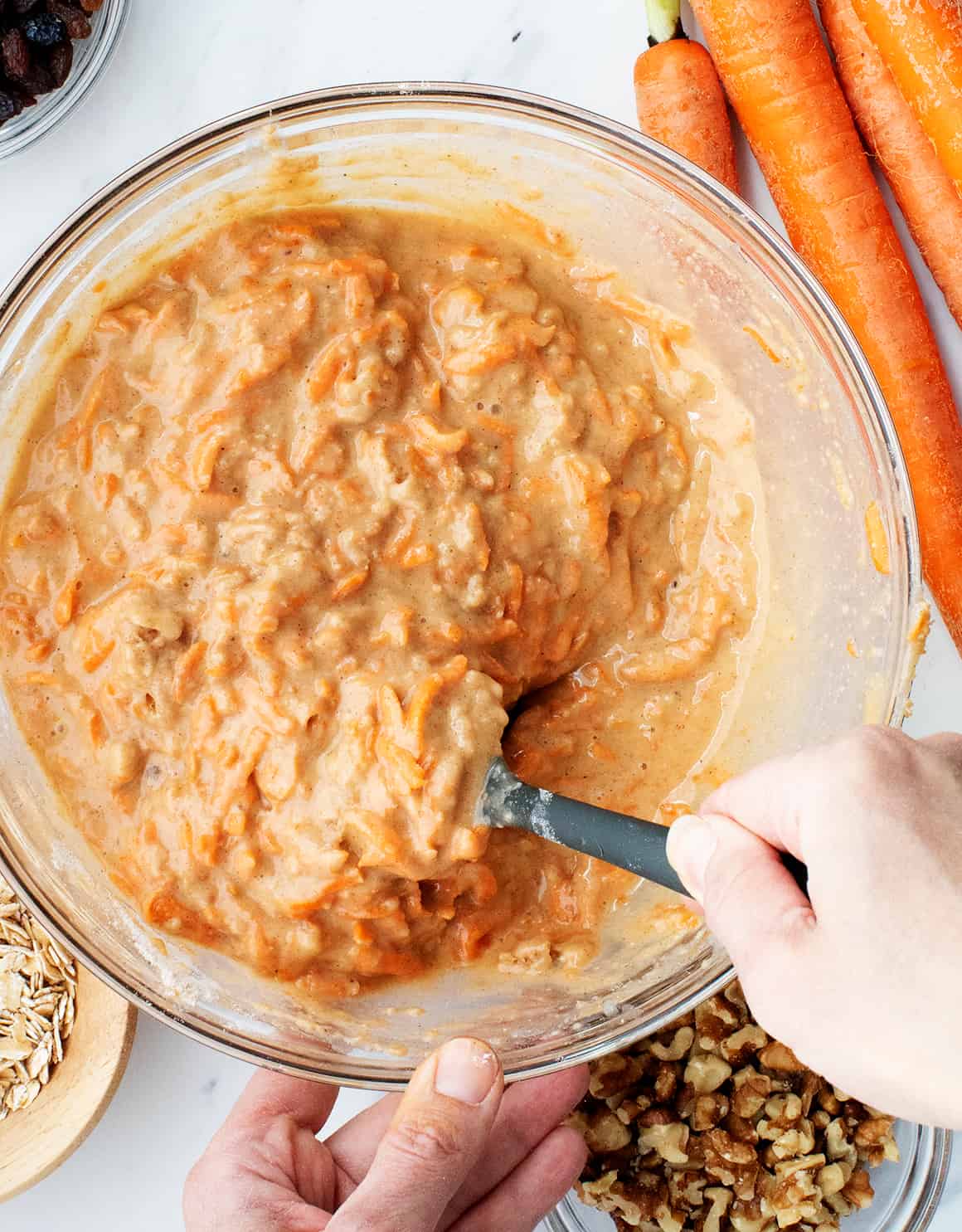 Hand using spatula to mix batter for carrot muffins