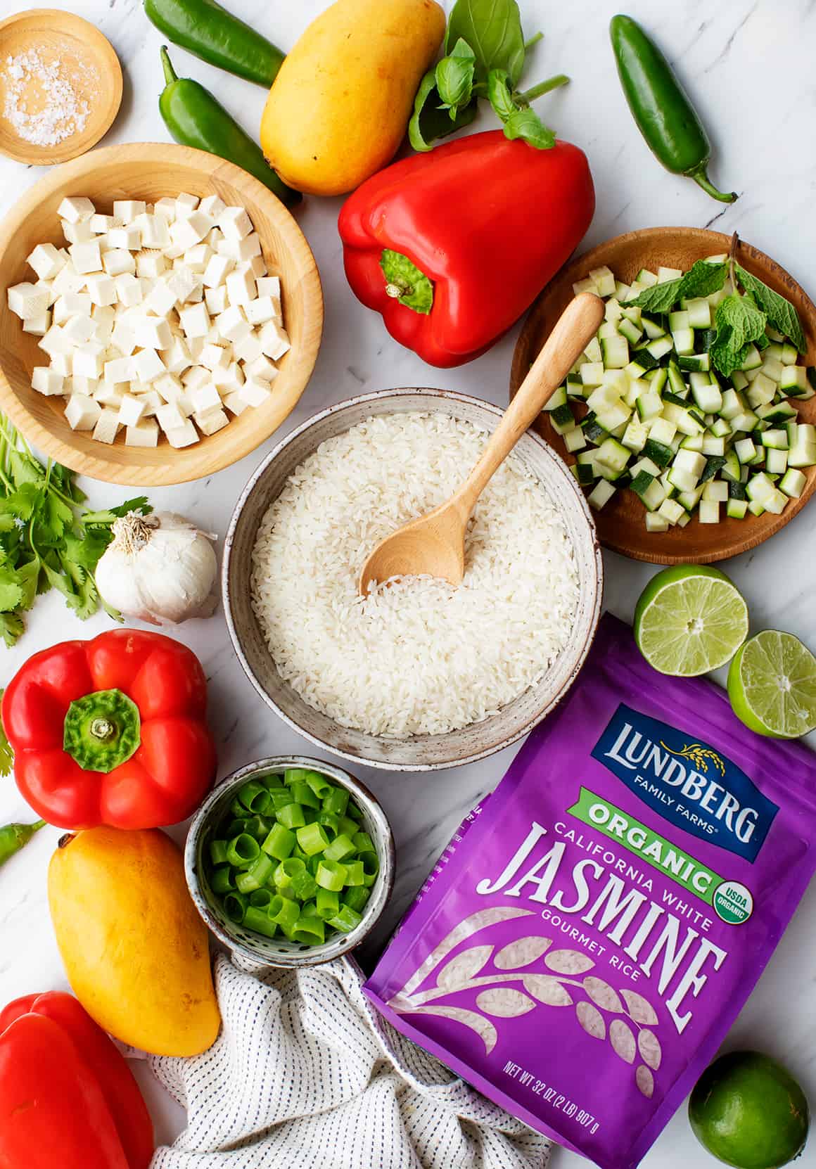 Bell peppers, bag of Lundberg jasmine rice, mangos, scallions, diced zucchini and tofu, jalapeños, and herbs on marble