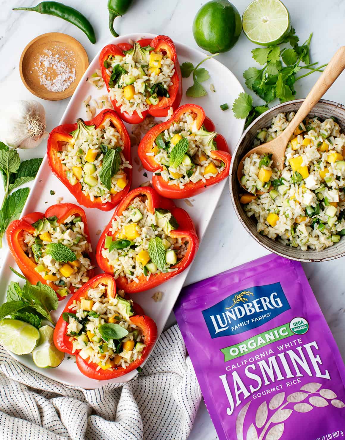 Coconut rice-stuffed peppers on a platter with bowl of coconut rice filling and bag of Lundberg jasmine rice