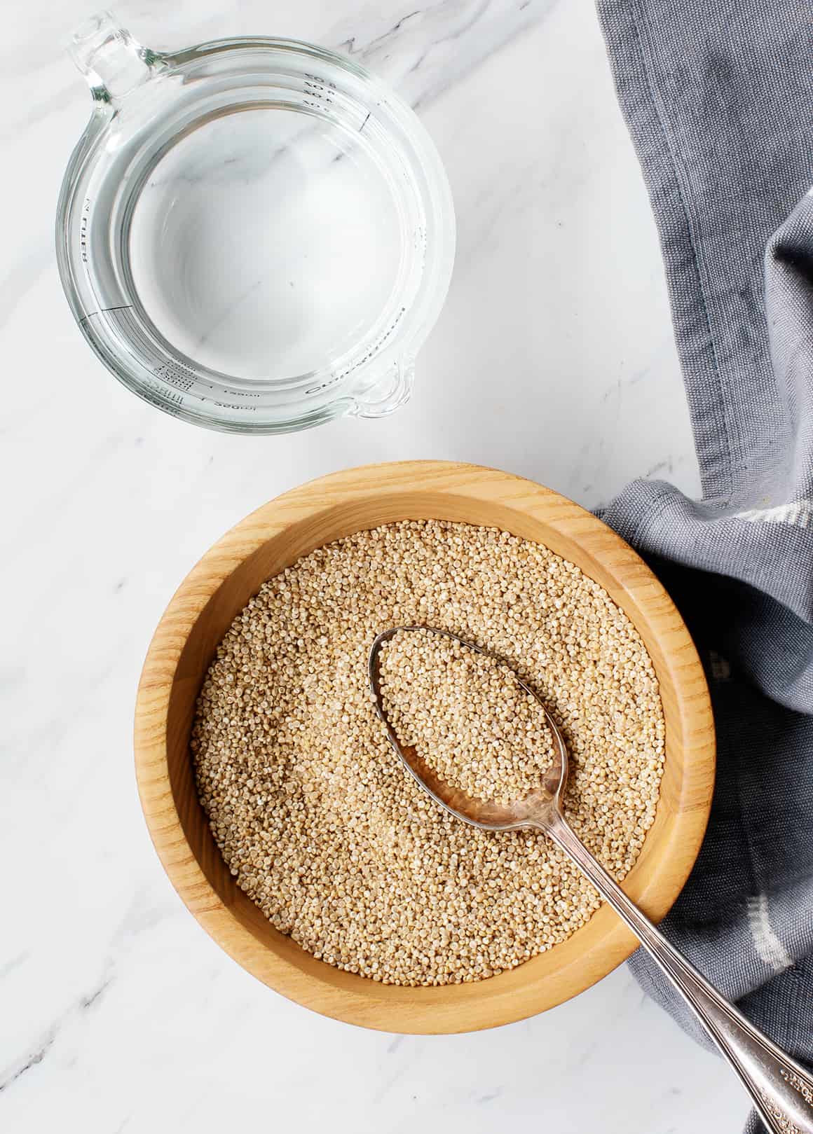 Bowl of dry quinoa and glass liquid measuring cup filled with water