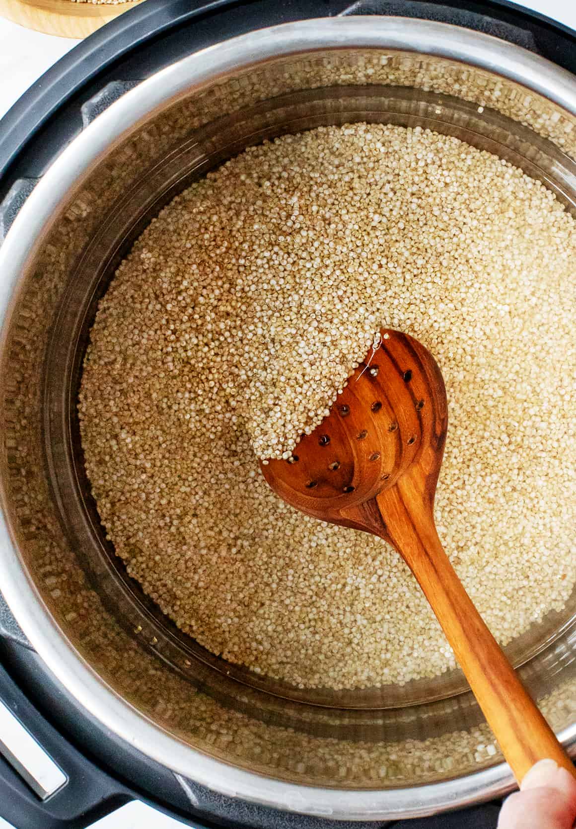 Stirring quinoa and water in Instant Pot with wooden spoon