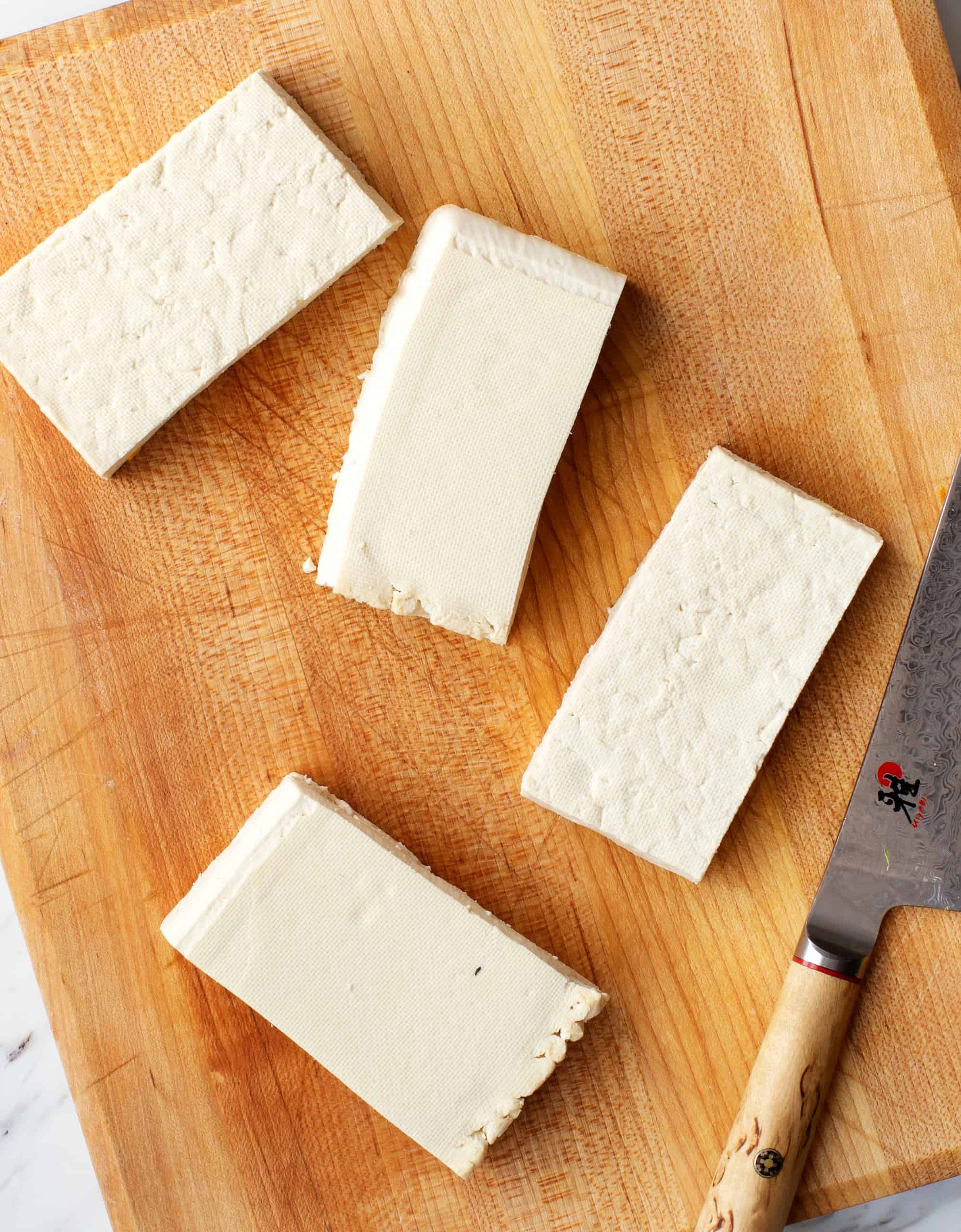 Pressed tofu slabs on cutting board with knife