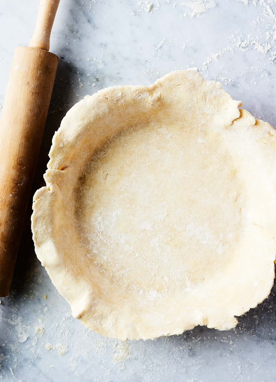 Easy pie crust recipe in pie plate next to wooden rolling pin