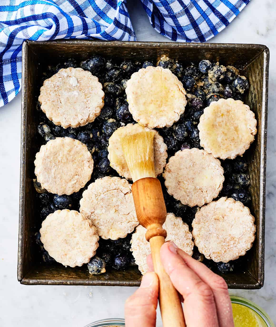 Brushing melted butter over blueberry cobbler biscuits