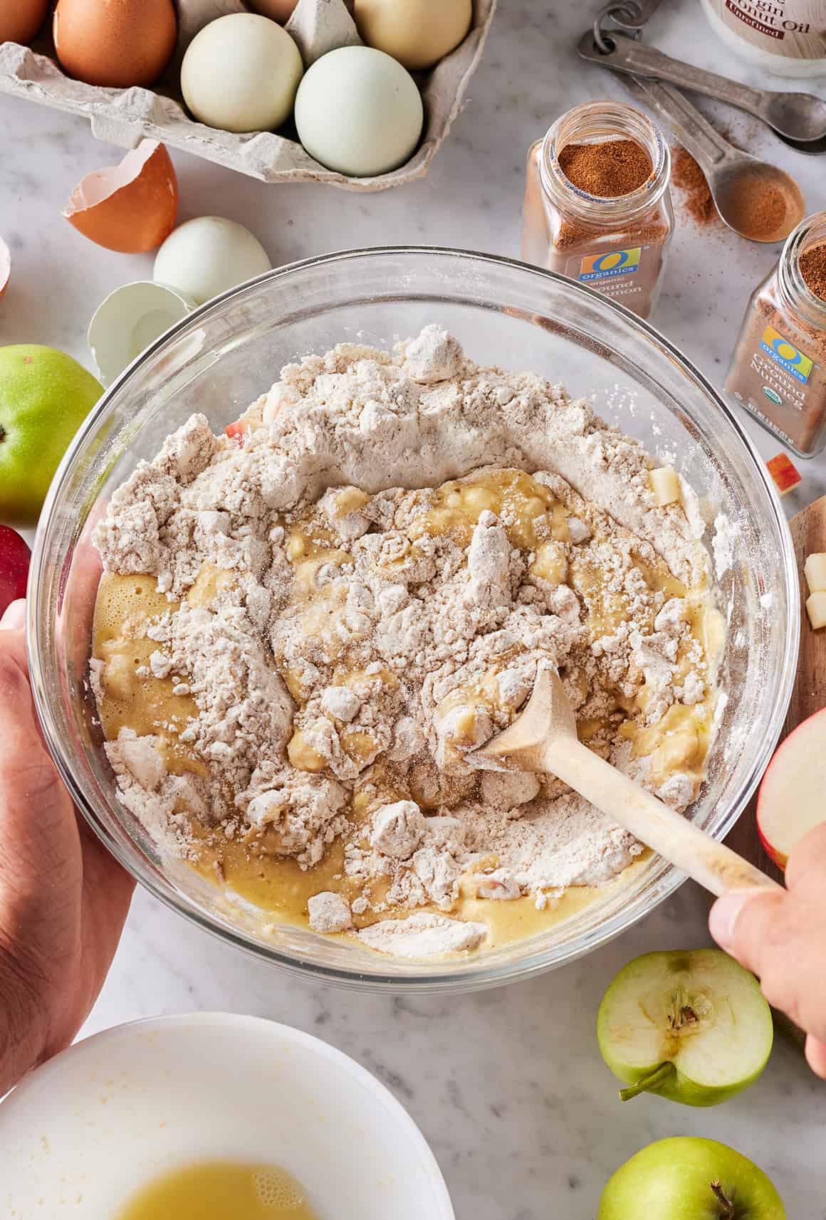Hand using wooden spoon to mix wet and dry ingredients in large glass bowl