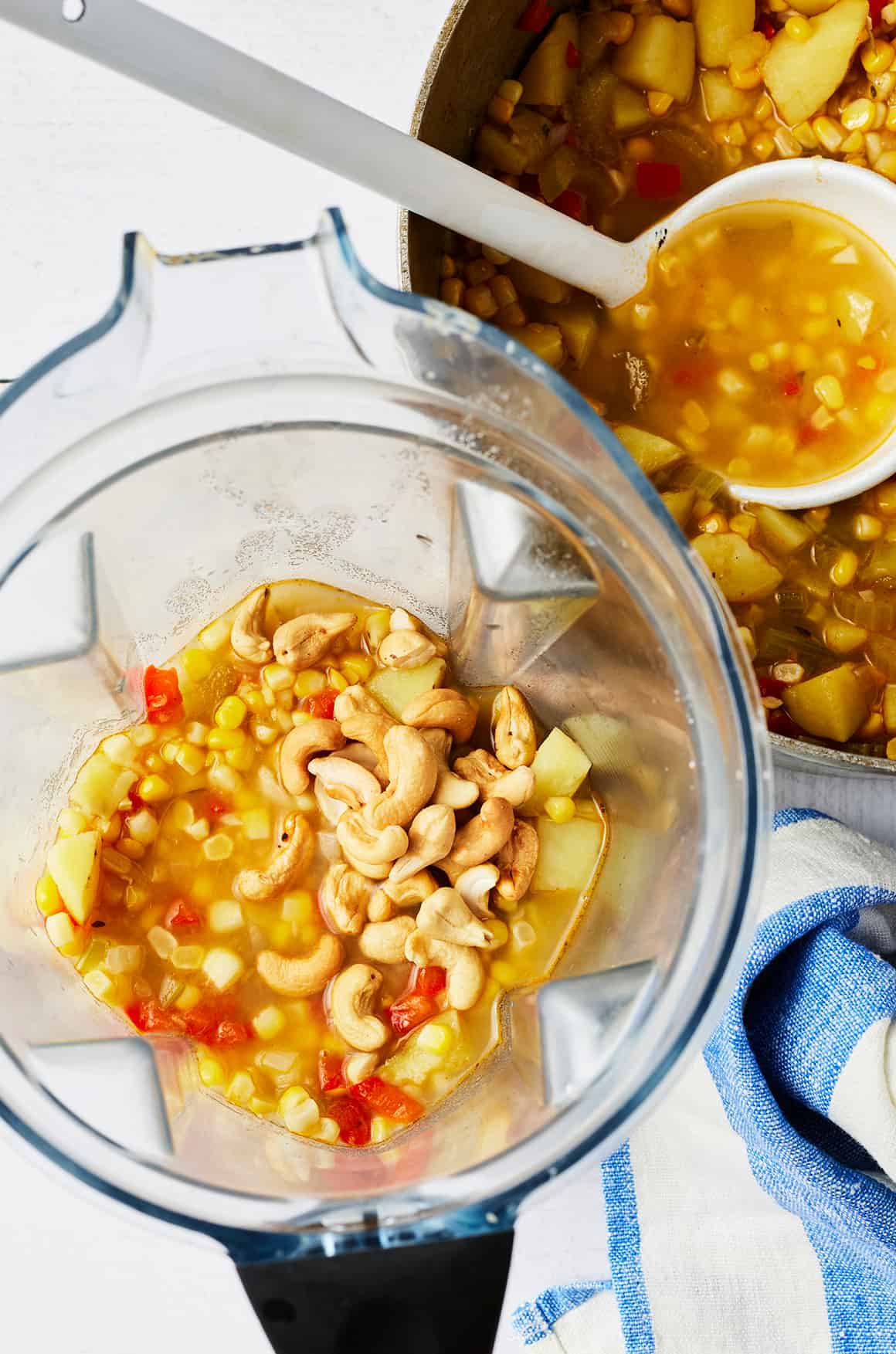 Soup and cashews in blender next to soup pot