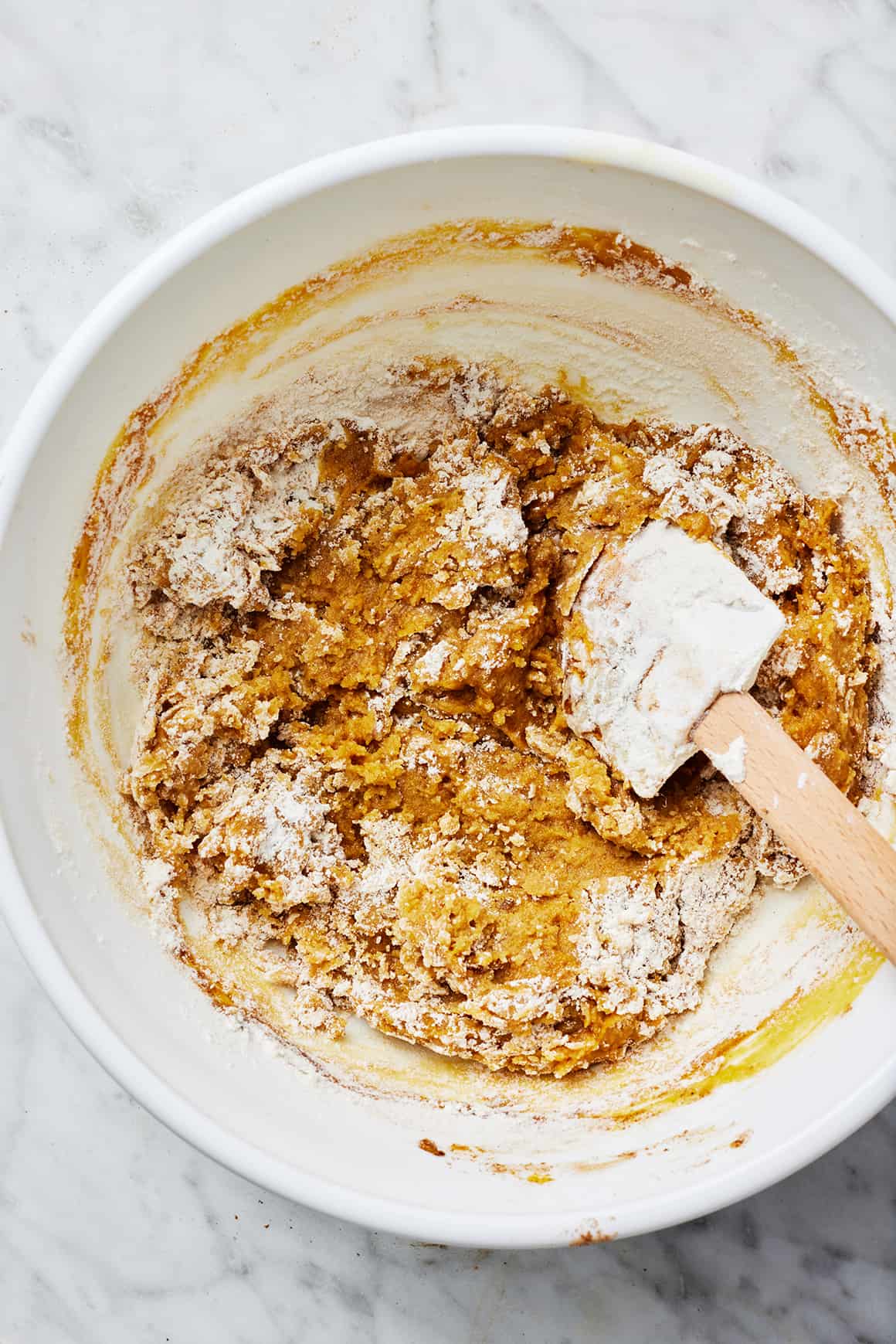 Partially mixed dry and wet ingredients in a mixing bowl with rubber spatula