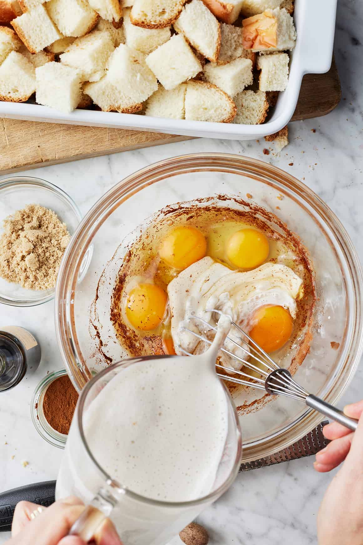 Hand whisking together almond milk, eggs, cinnamon, and nutmeg in a large bowl