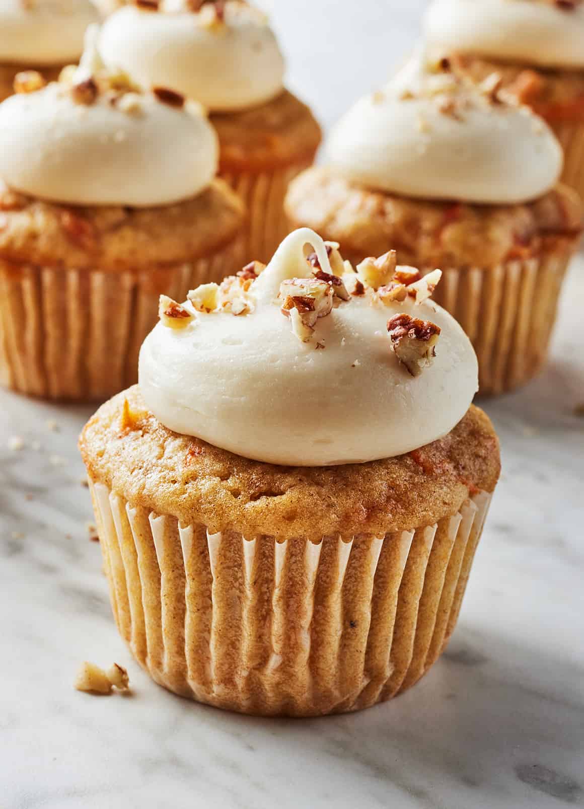 Carrot cake cupcakes topped with cream cheese frosting and chopped pecans