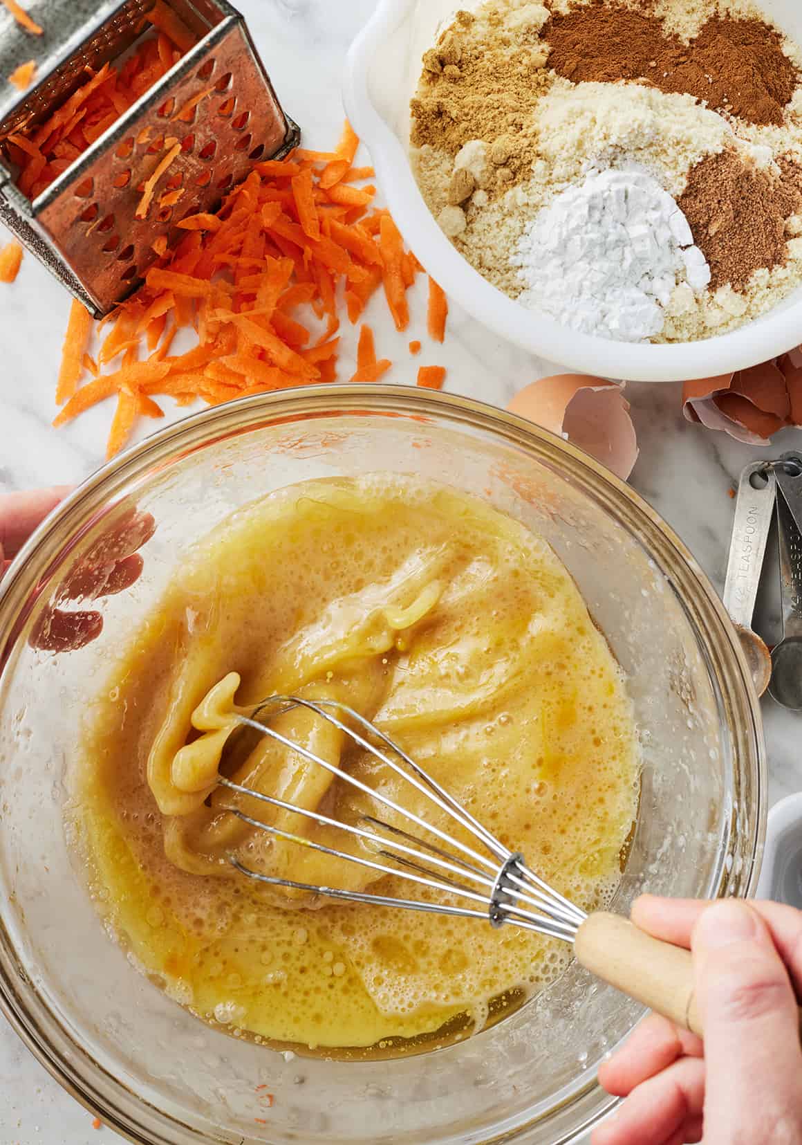 Hand whisking together wet ingredients in glass mixing bowl