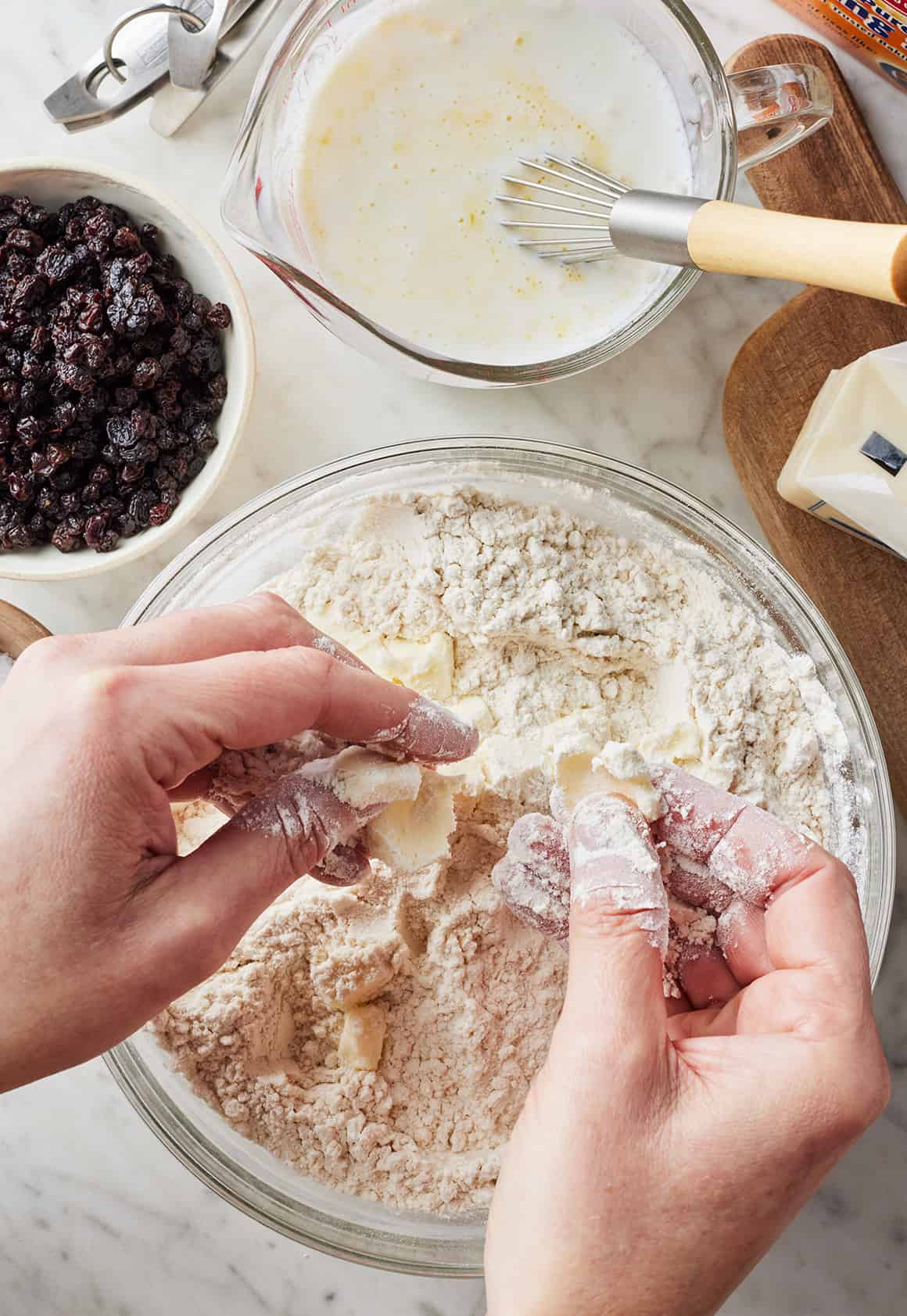 Hands working cubed butter into flour in a mixing bowl