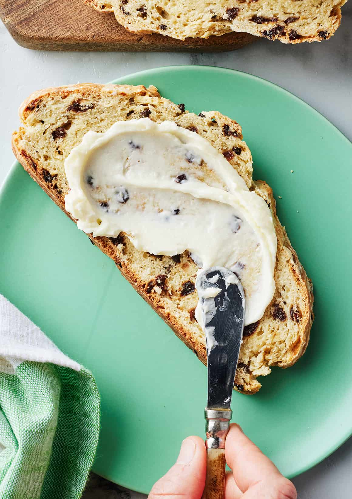 Hand using knife to spread butter on slice of Irish soda bread on green plate