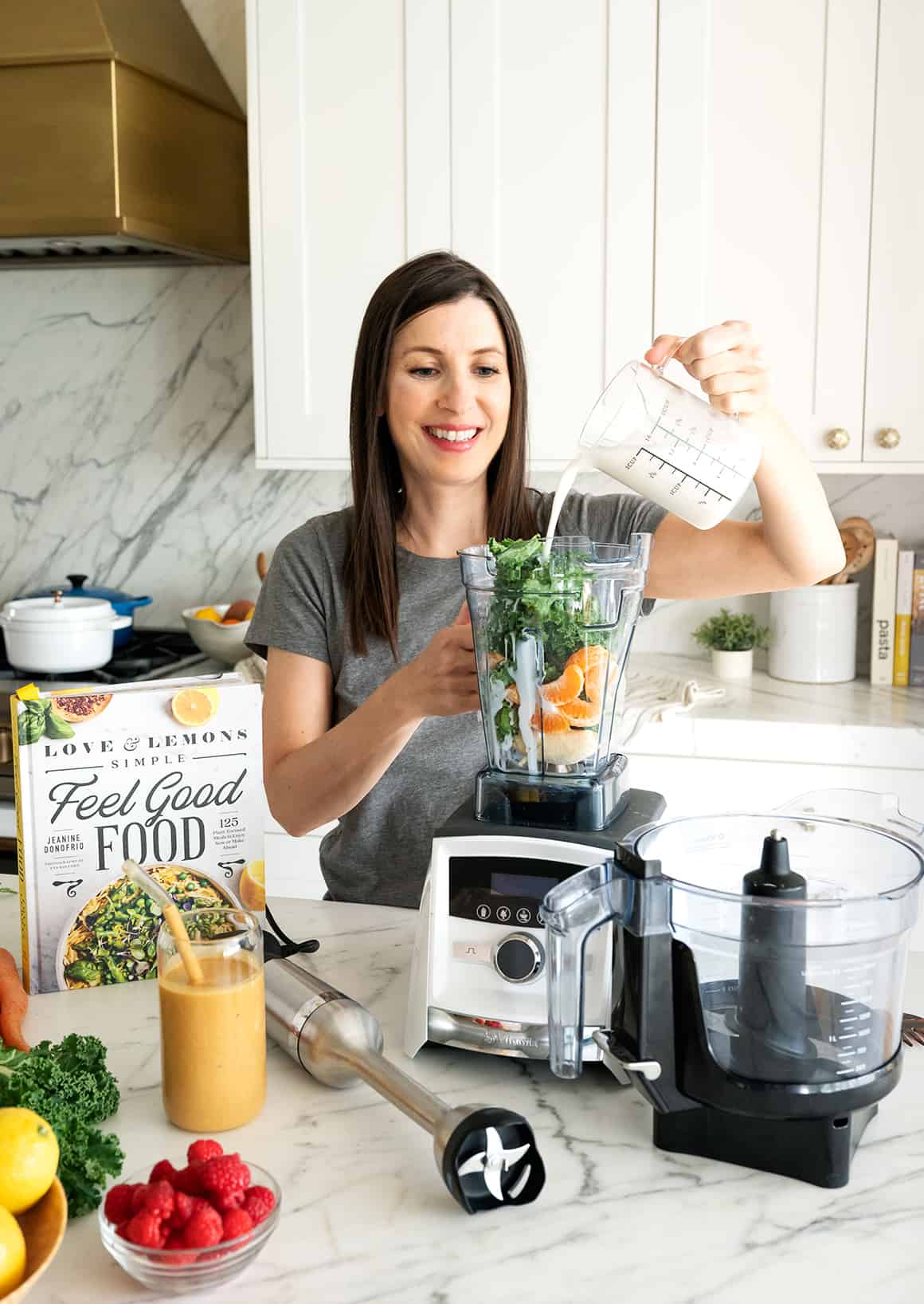 Jeanine pouring almond milk into Vitamix blender filled with kale, banana, and orange segments