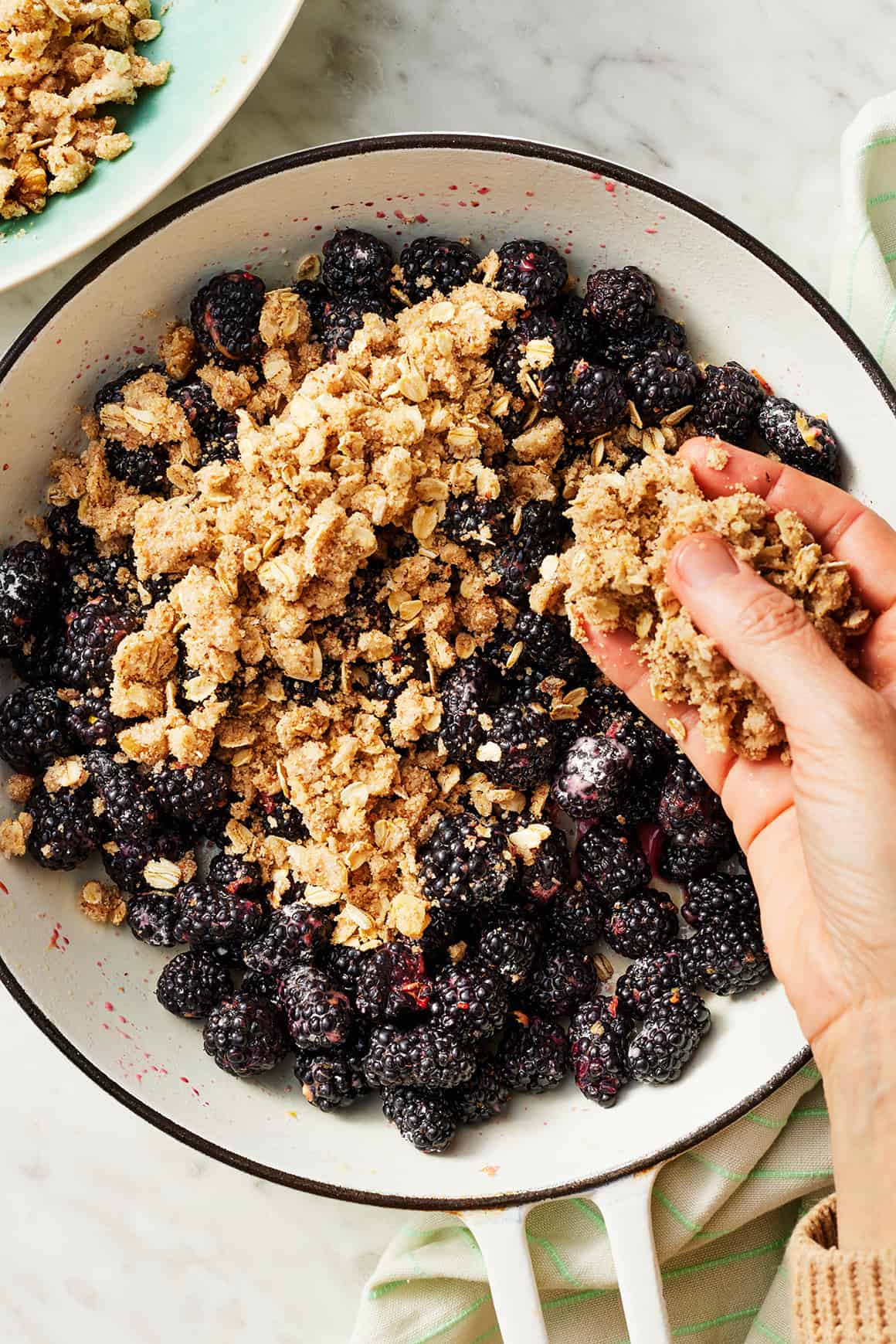 Sprinkling crumble topping over blackberry crisp