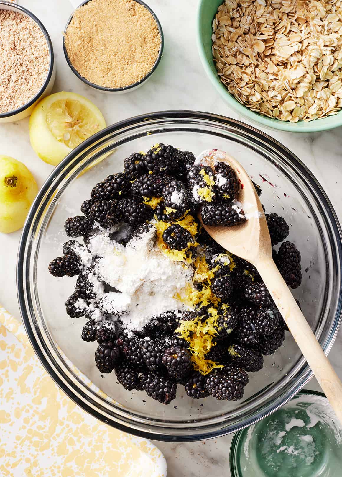 Fresh blackberries in glass mixing bowl with cornstarch, lemon zest, and wooden spoon