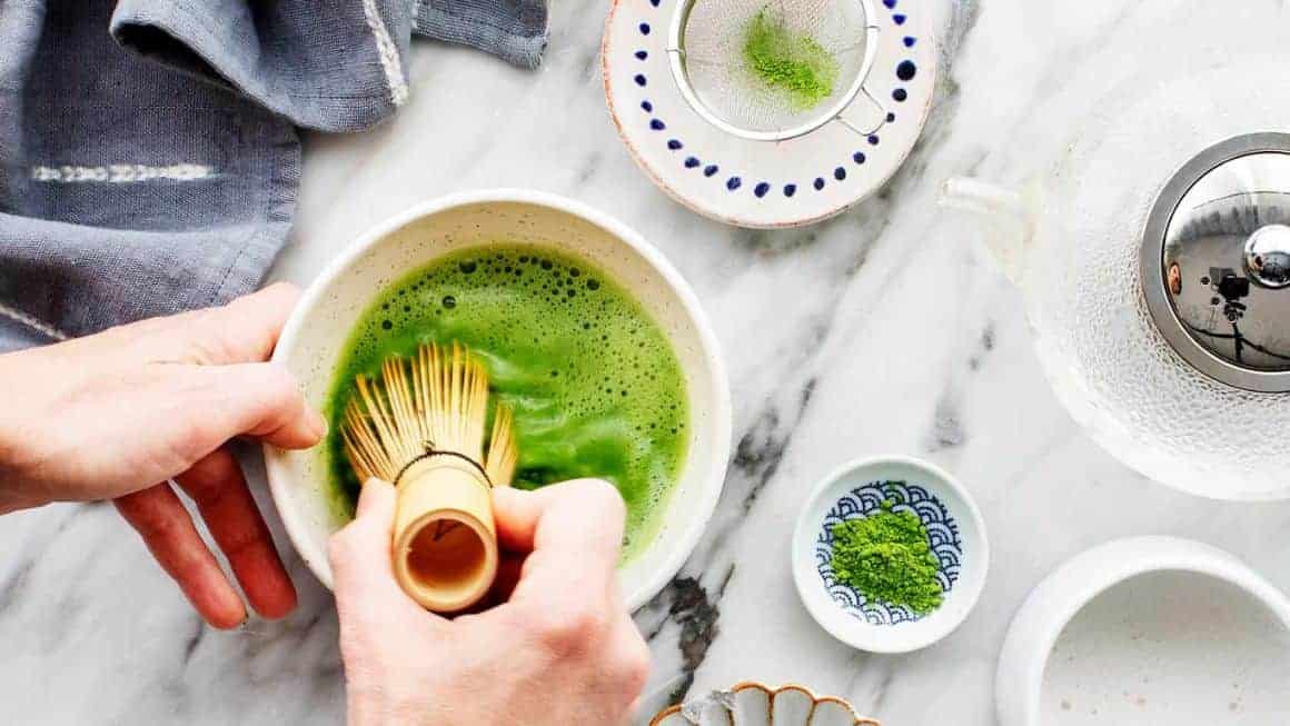 Making matcha tea in bowl with bamboo whisk