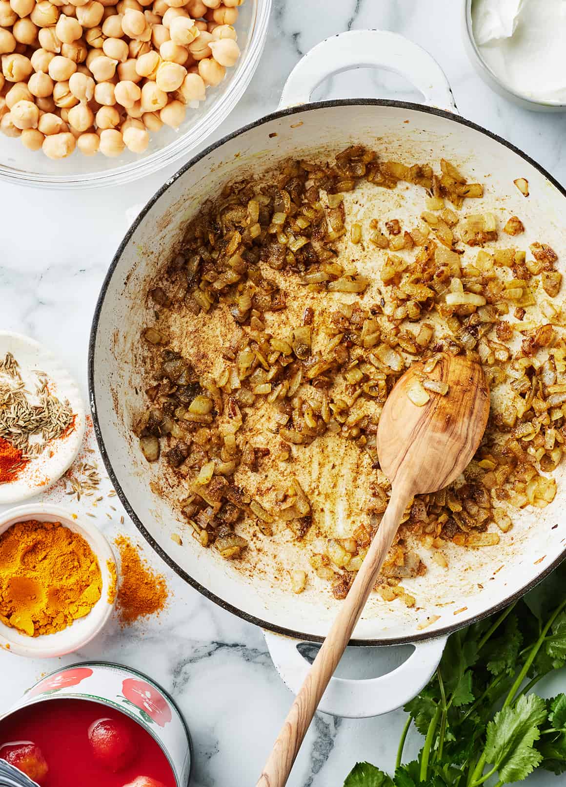 Onions and spices cooking in a skillet with wooden spoon