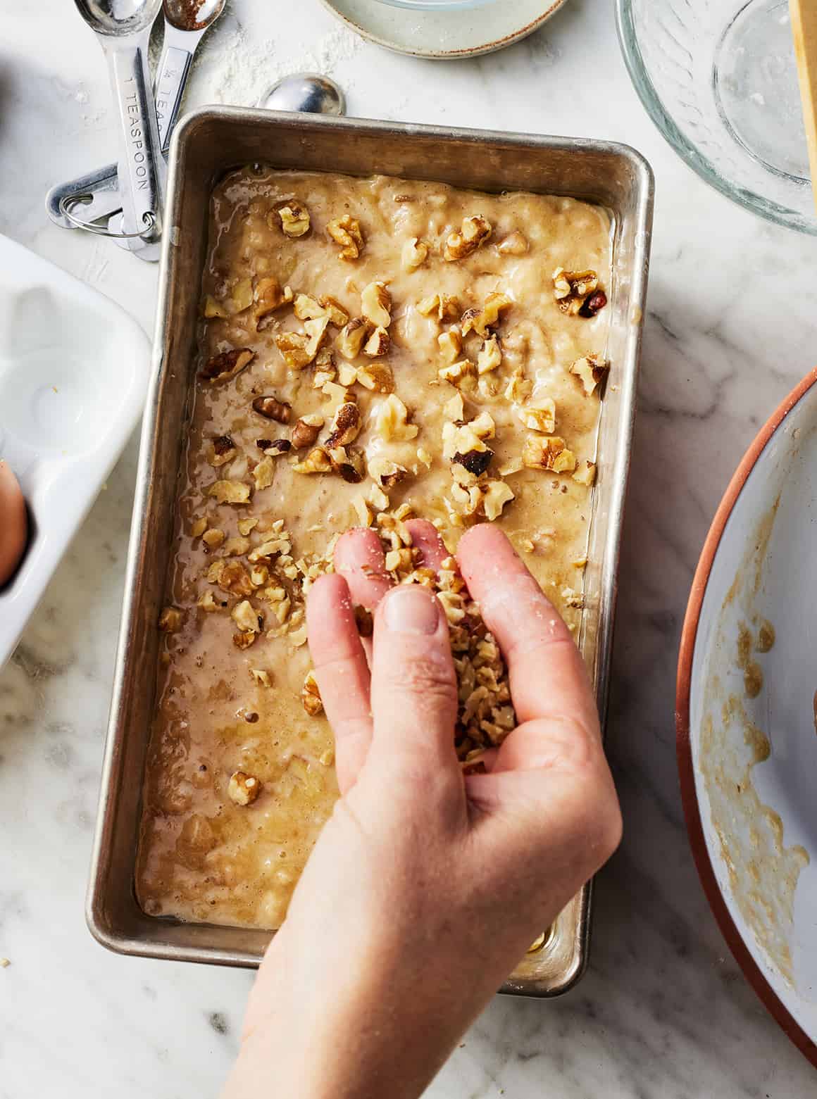 Sprinkling walnuts over moist banana bread batter in loaf pan