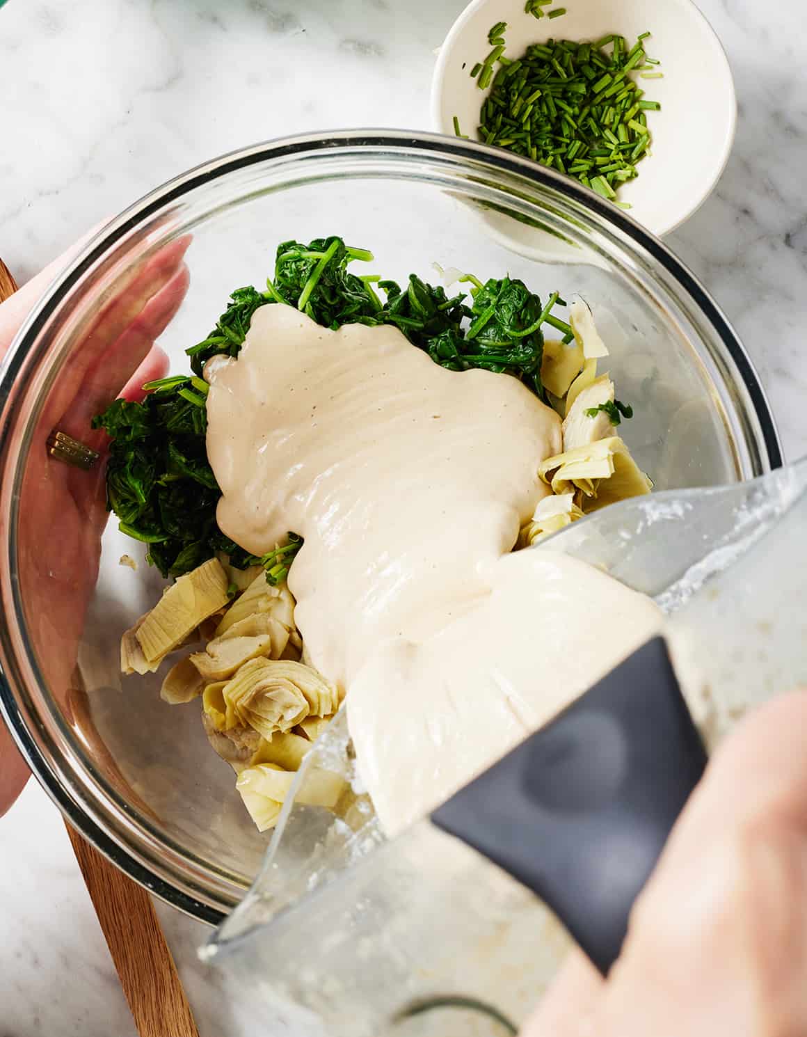 Pouring cashew cream over vegetables in glass bowl
