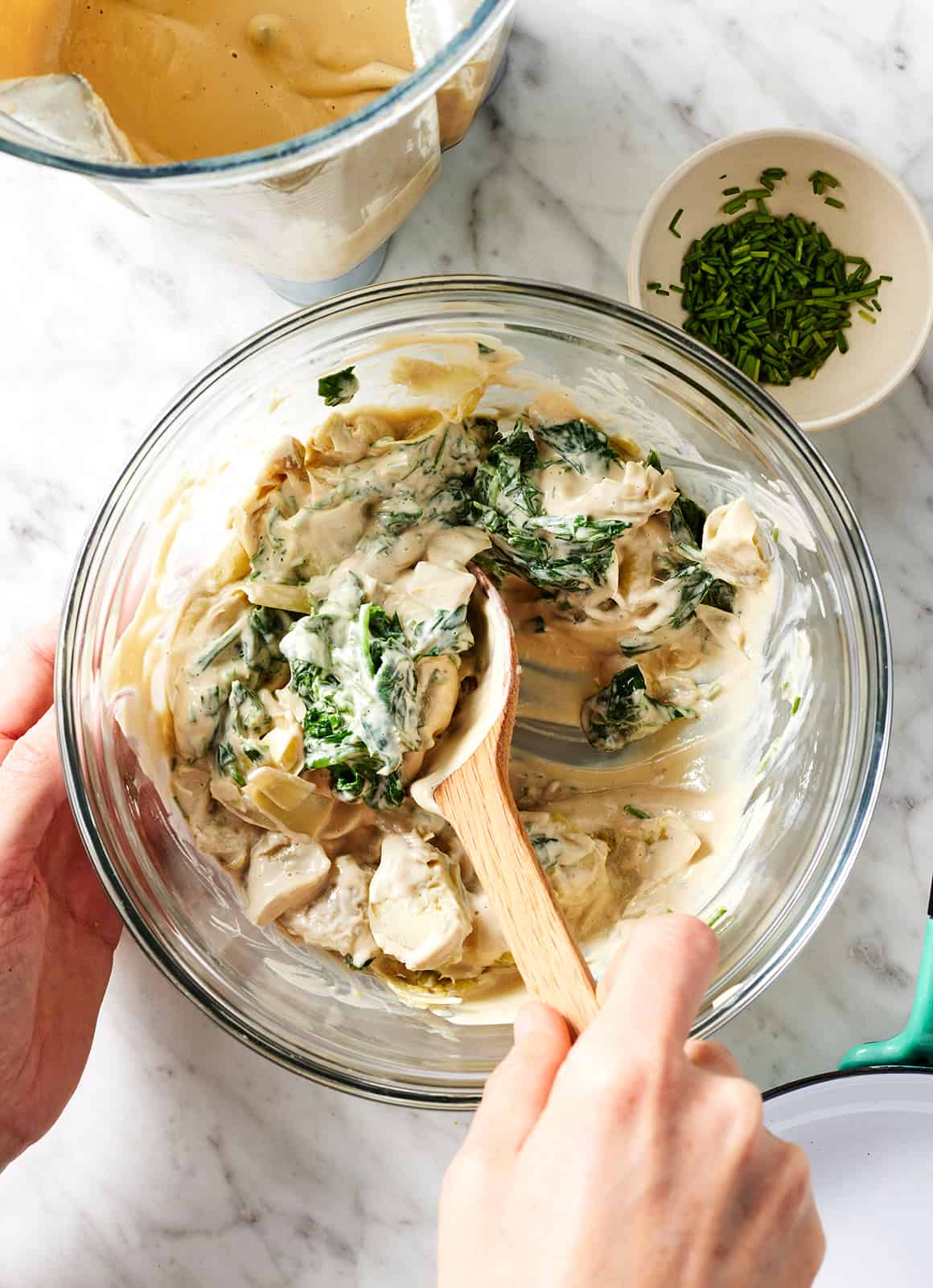 Stirring creamy cashew mixture and vegetables in glass bowl