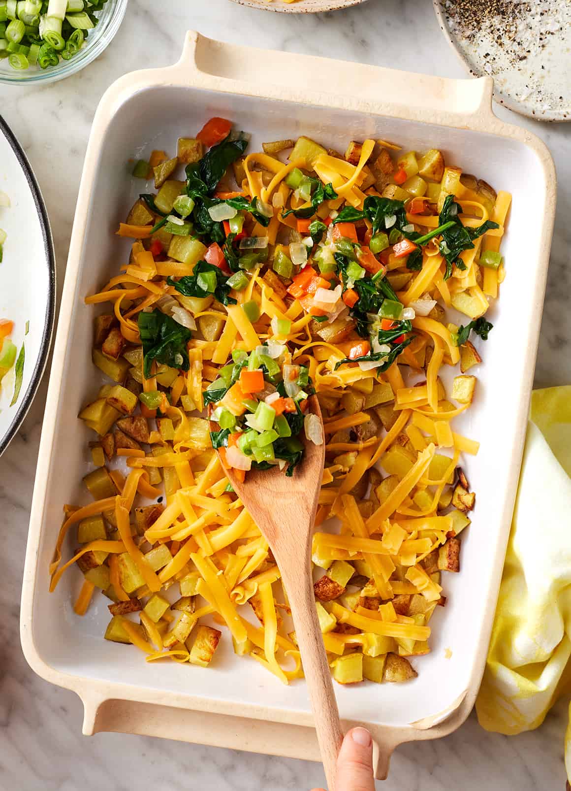 Layering vegetables, cheese, and potatoes in baking dish