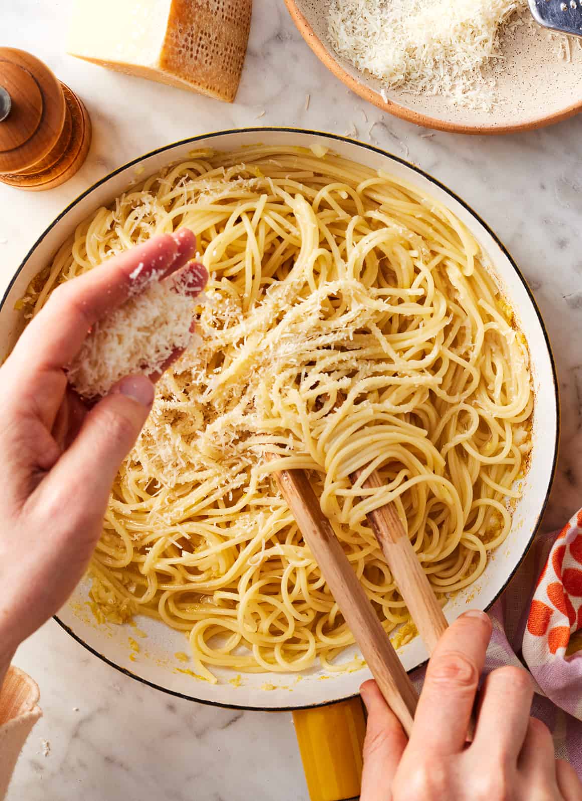Adding grated Parmesan cheese to skillet with spaghetti