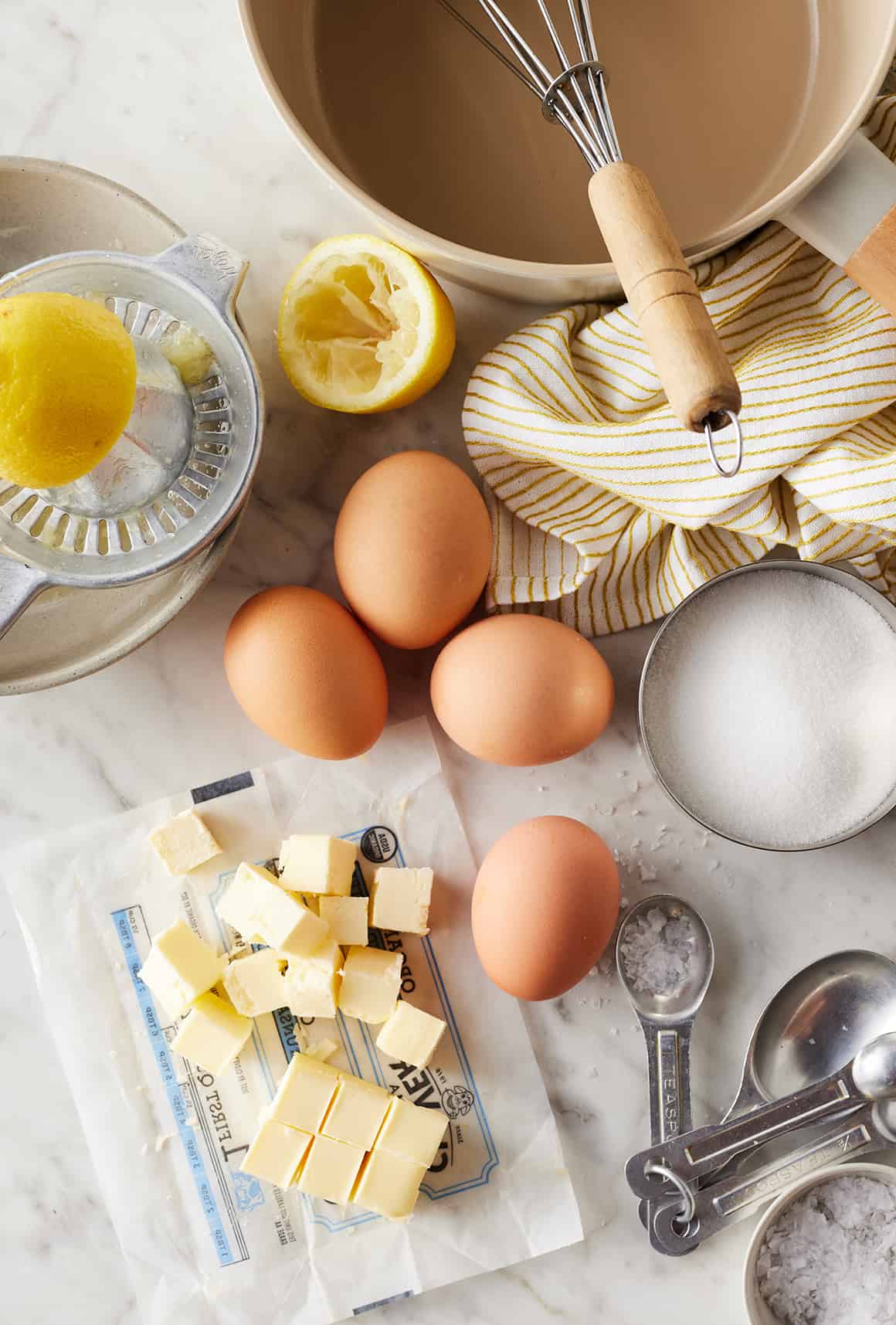Lemons, whole eggs, sugar, and cubed butter on countertop