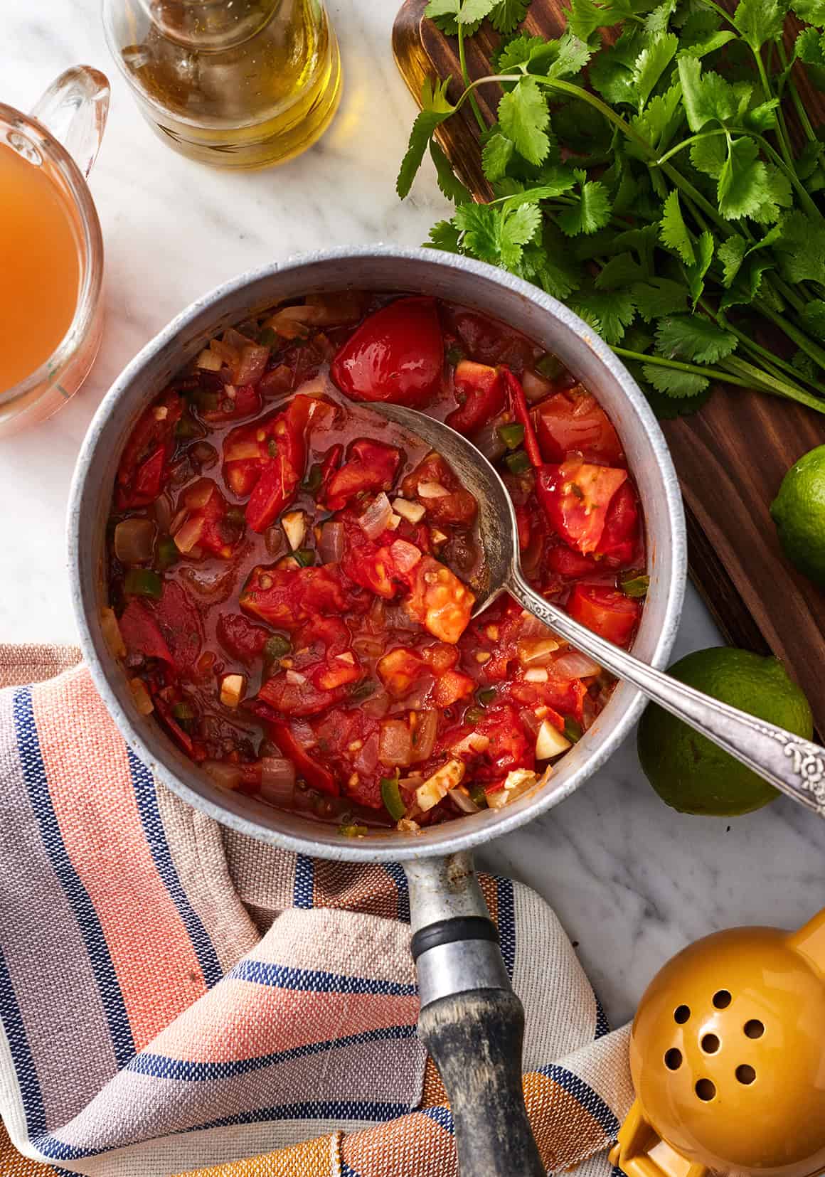Cooked tomatoes, onion, garlic, and jalapenos in saucepan with spoon