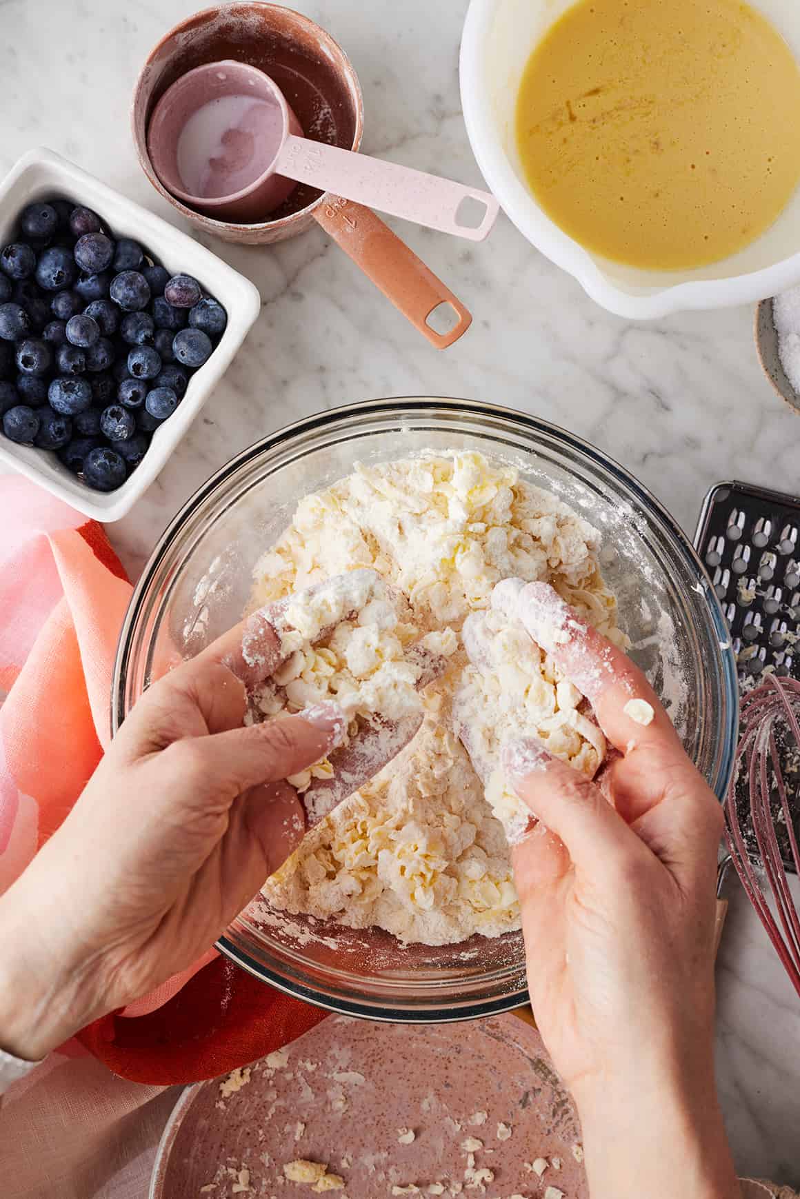 Hands combining frozen grated butter with flour