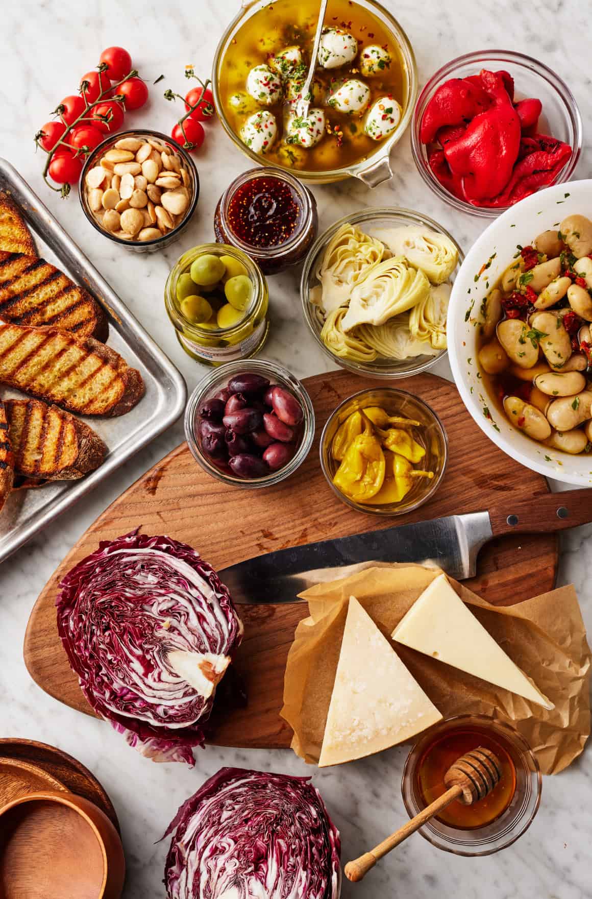 Olives, pepperoncini, marinated gigante beans, artichoke hearts, marinated mozzarella, roasted red peppers, cherry tomatoes, radicchio, cheese, and crostini on countertop